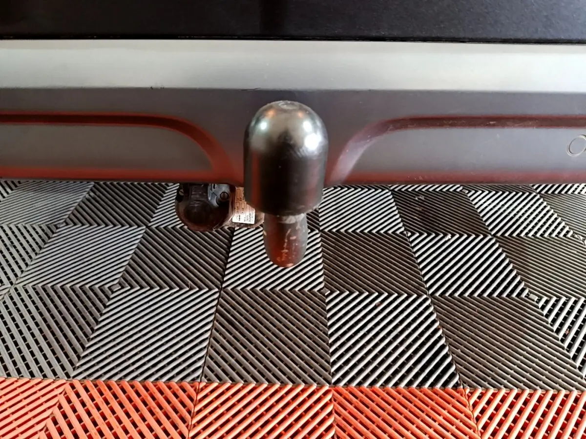 Gros plan sur l'attelage noir sous le pare-chocs arrière du Renault Kadjar rouge, posé sur un sol à damiers noir et rouge.