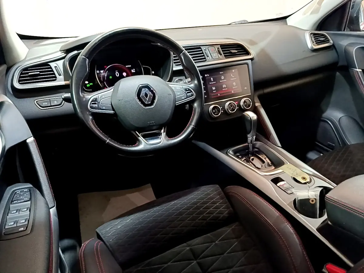 Vue intérieure côté conducteur du Renault Kadjar rouge, mettant en valeur le volant cuir multifonctions et la console centrale avec écran tactile.
