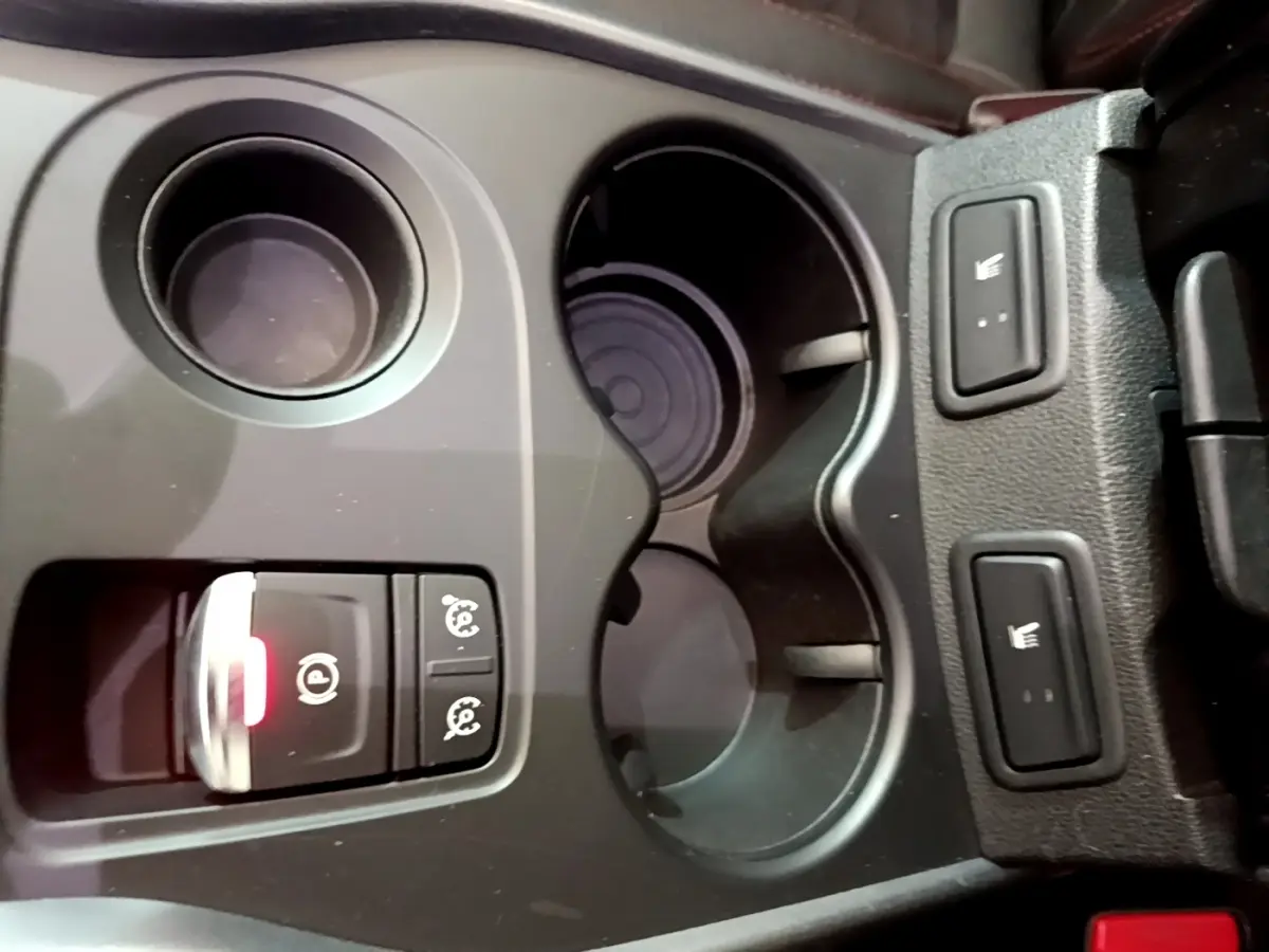 Gros plan sur la console centrale noire du Renault Kadjar rouge, avec porte-gobelets et boutons de sièges chauffants.