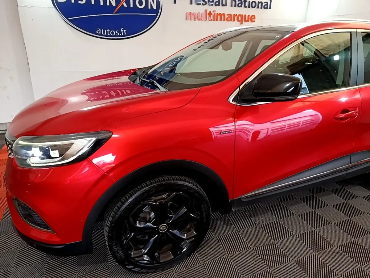 Vue de profil avant droit d’un Renault Kadjar rouge avec jantes noires brillantes et rétroviseur noir.