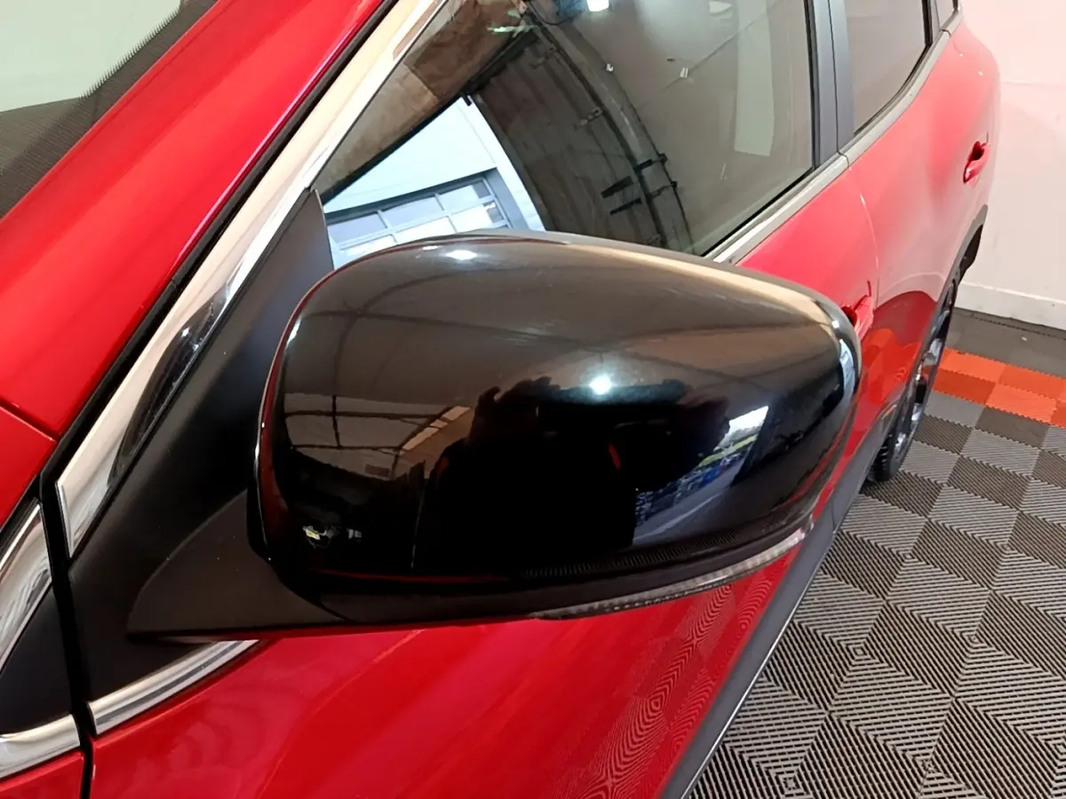 Gros plan sur le rétroviseur noir côté gauche d’un Renault Kadjar rouge, avec reflet de l’environnement intérieur.