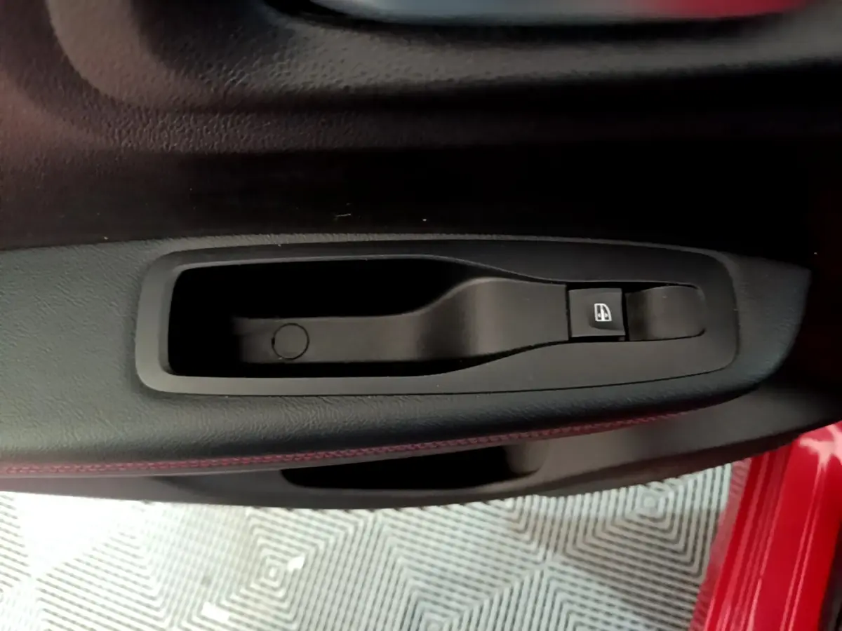 Gros plan sur la poignée intérieure côté gauche d’une Renault Kadjar rouge, avec bouton de commande de vitre électrique.