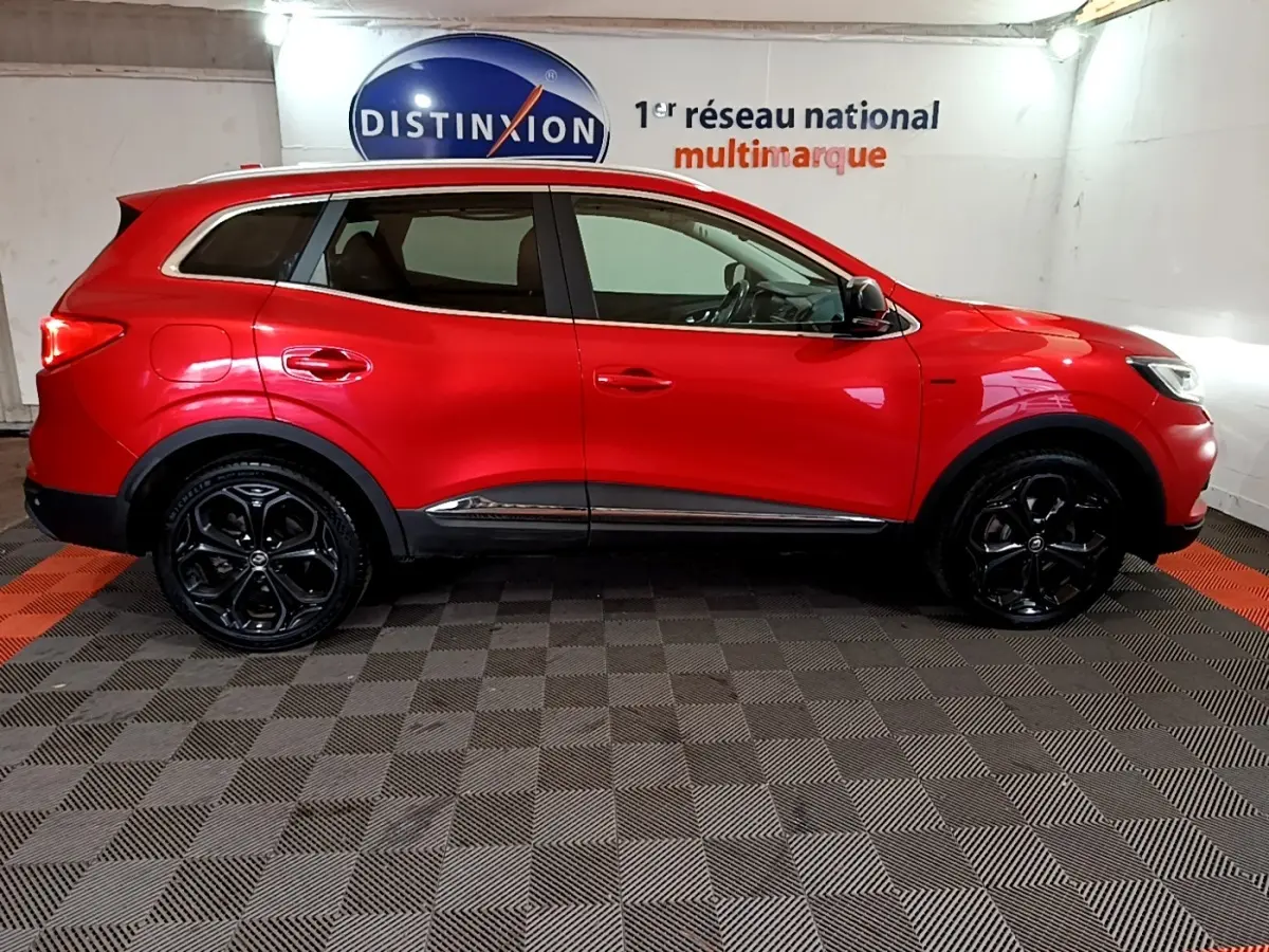 Profil droit d’un Renault Kadjar rouge SL Black Edition avec jantes noires et détails chromés, en intérieur showroom.
