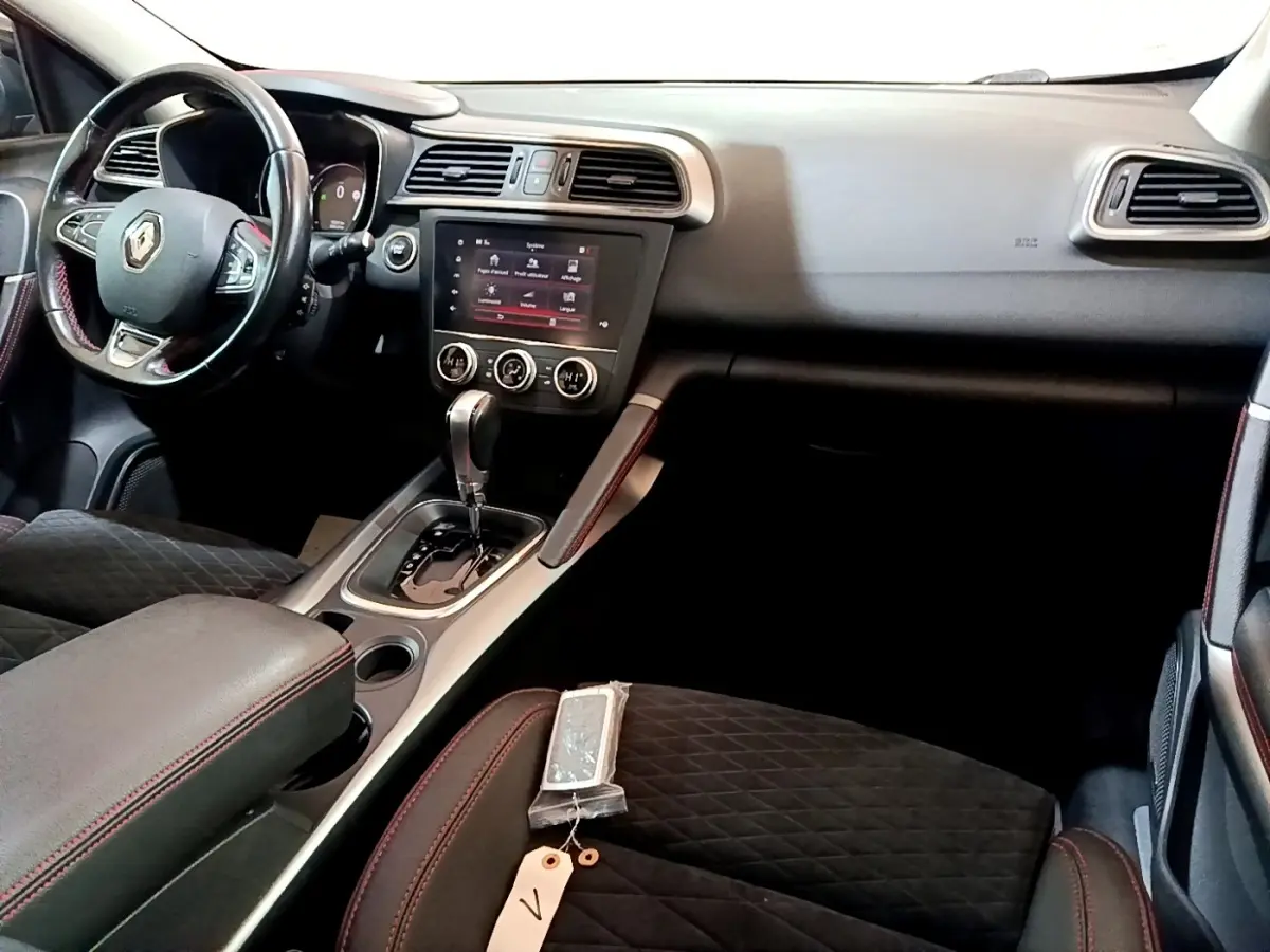 Vue intérieure côté conducteur du Renault Kadjar 2019, tableau de bord noir avec écran tactile et sellerie noire à surpiqûres rouges.