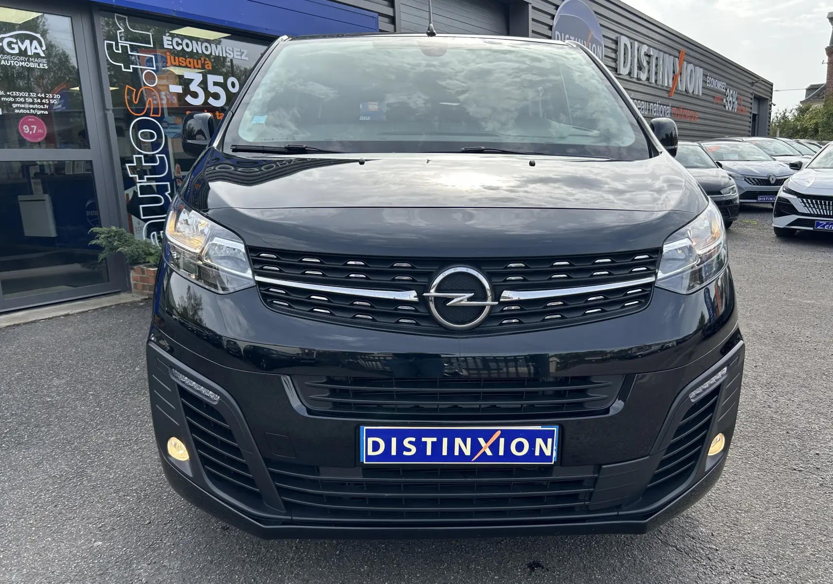 Vue avant d'un Opel Vivaro Combi noir 2022 avec calandre distinctive et phares allumés, stationné devant un concessionnaire.