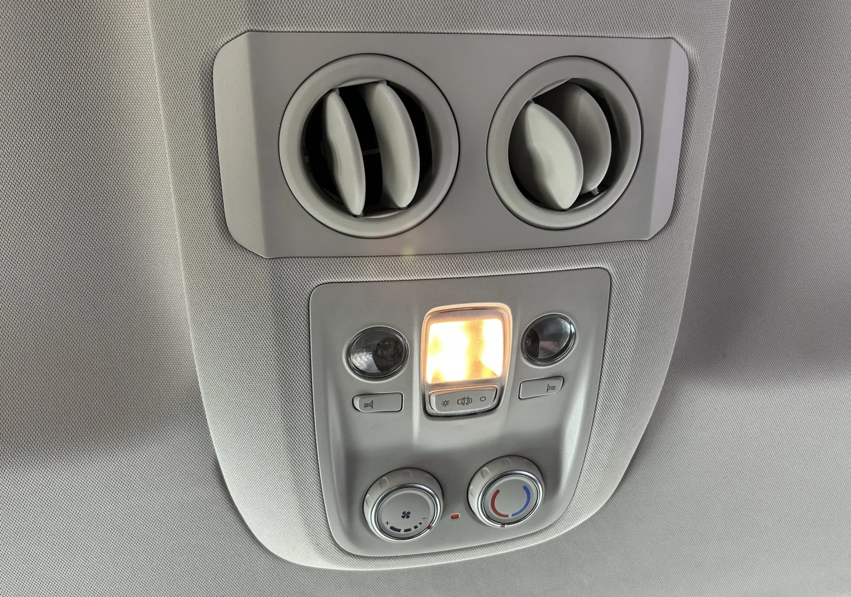 Vue intérieure en gros plan du plafonnier gris avec commandes de climatisation et éclairage allumé dans un Opel Vivaro Combi noir.