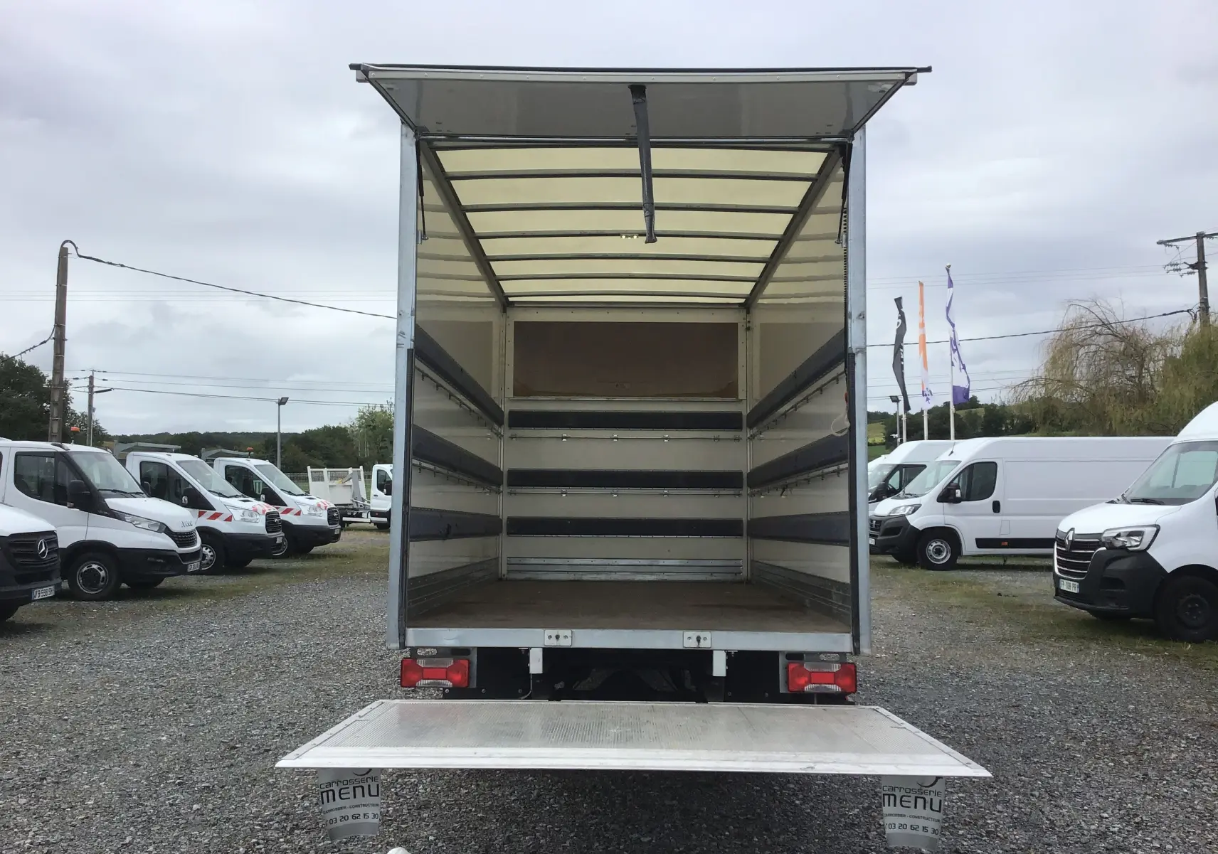 Vue arrière d’un Iveco Daily blanc 2022 avec caisse ouverte de 20m3 et hayon élévateur déployé sur parking