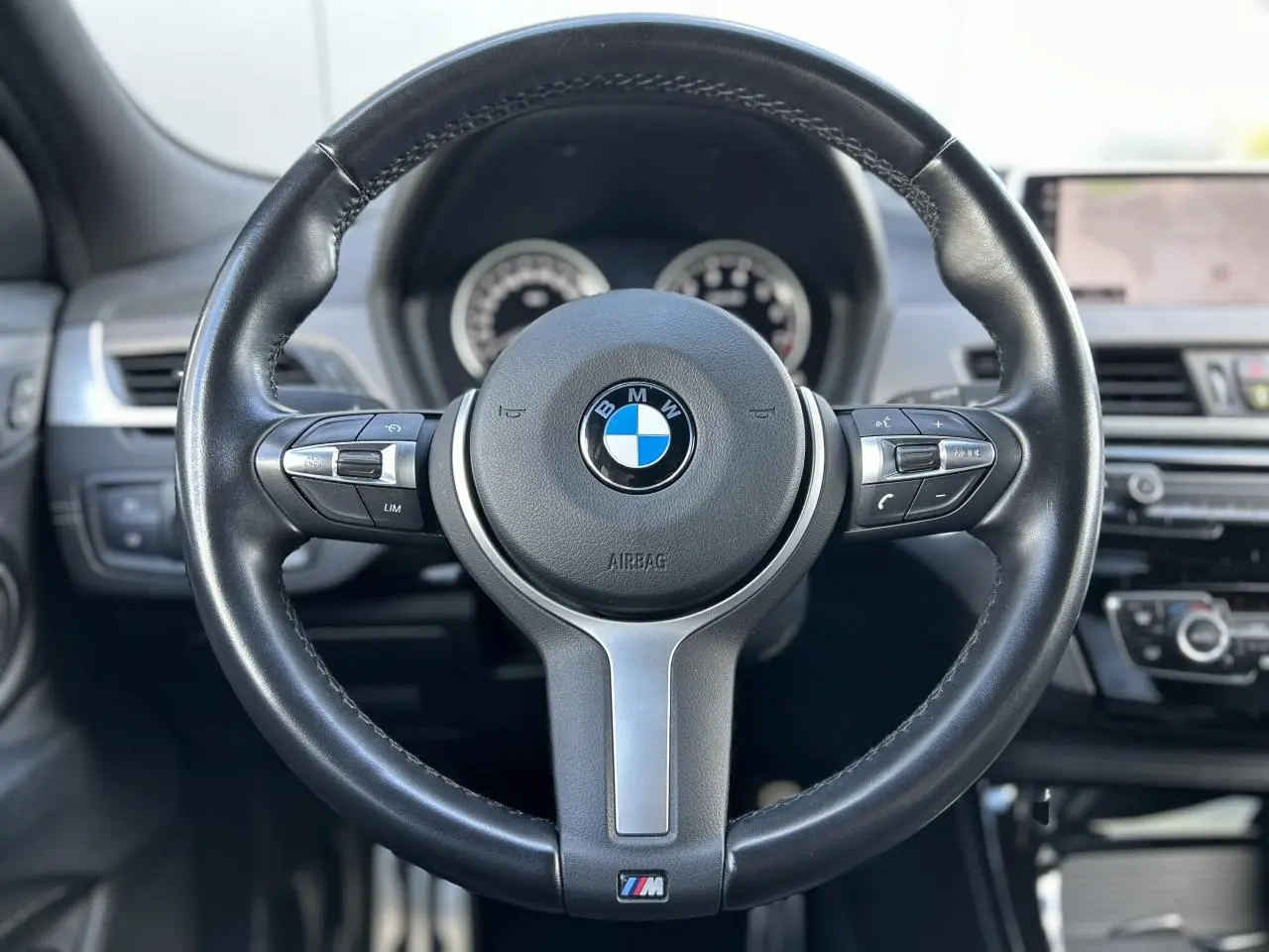 Volant cuir M noir de BMW X2 F39 2021, vue frontale centrée sur le volant avec tableau de bord et écran GPS flous en arrière-plan