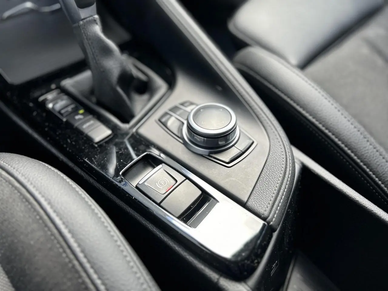 Gros plan sur la console centrale noire du BMW X2 F39, mettant en valeur la commande de frein à main électrique et le sélecteur rotatif.