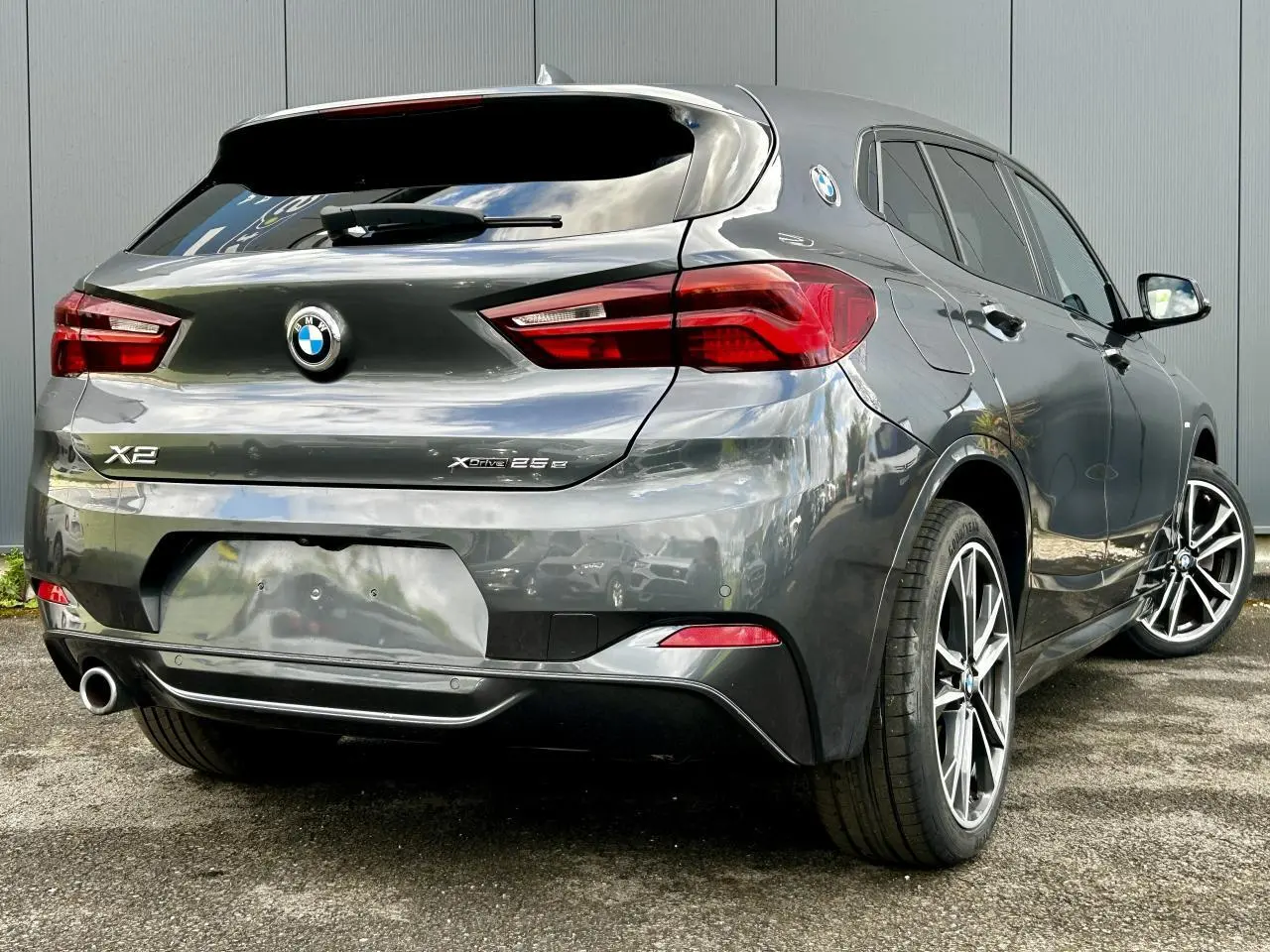 Vue 3/4 arrière droite d'une BMW X2 Gris Mineral avec jantes alliage bicolores et badges xDrive 25e visibles.