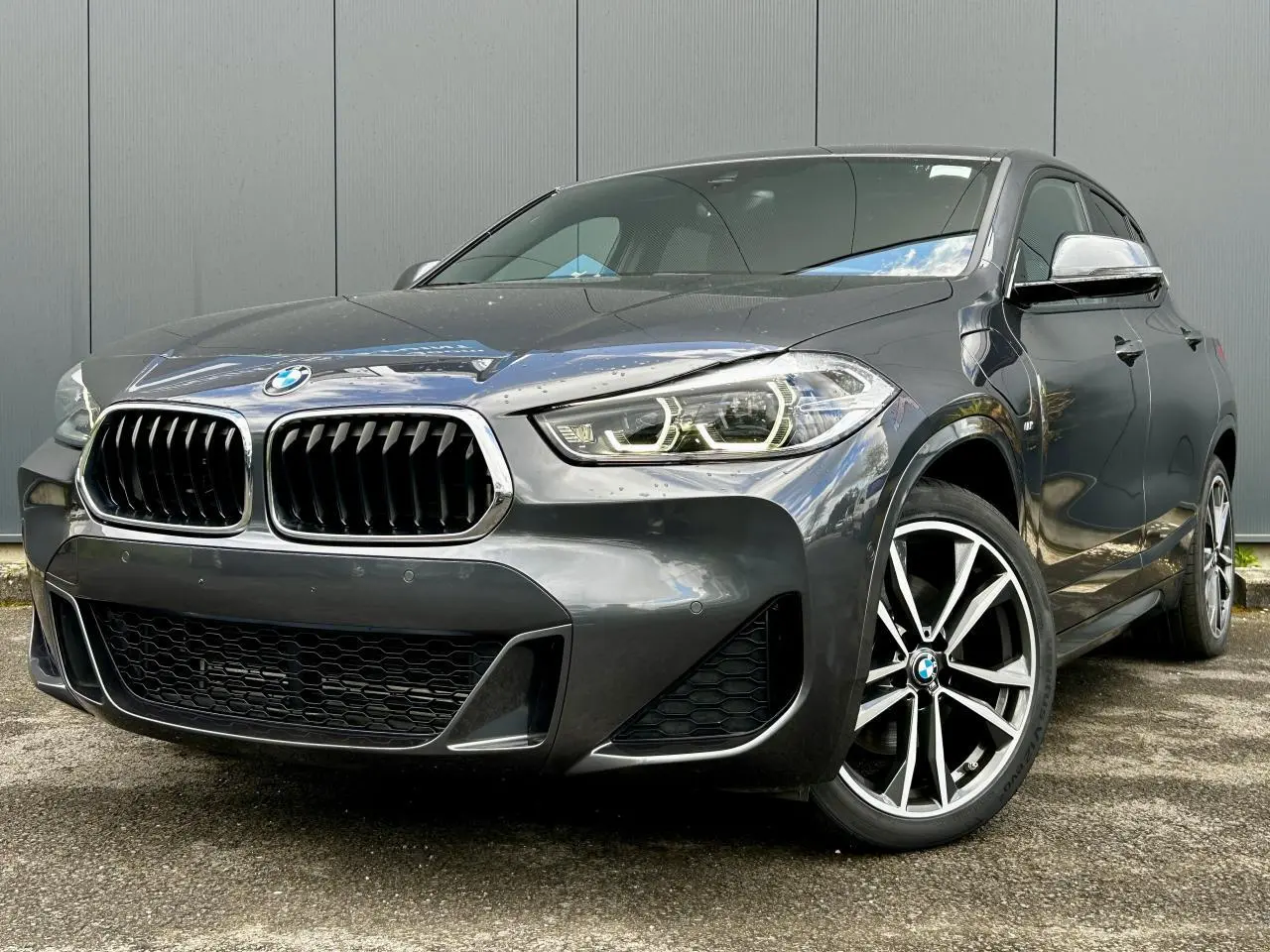 BMW X2 xDrive 25e gris Mineral vue 3/4 avant droit, avec jantes alliage bicolores et calandre M Sport distinctive.