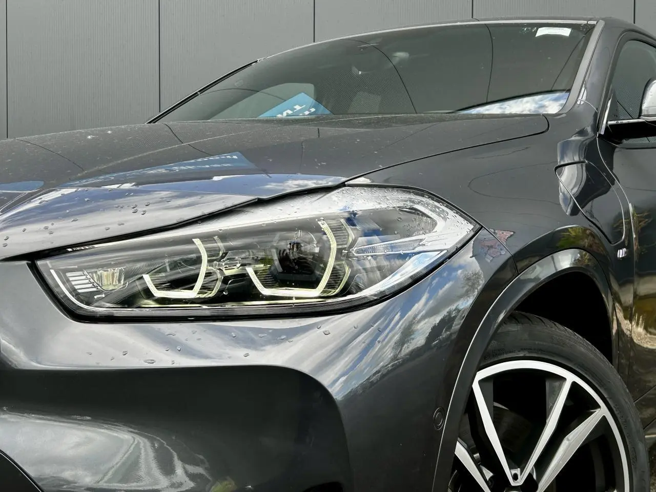 Gros plan sur l'avant droit d'un BMW X2 gris Mineral, mettant en valeur le phare LED et la jante alliage bicolore 19 pouces.
