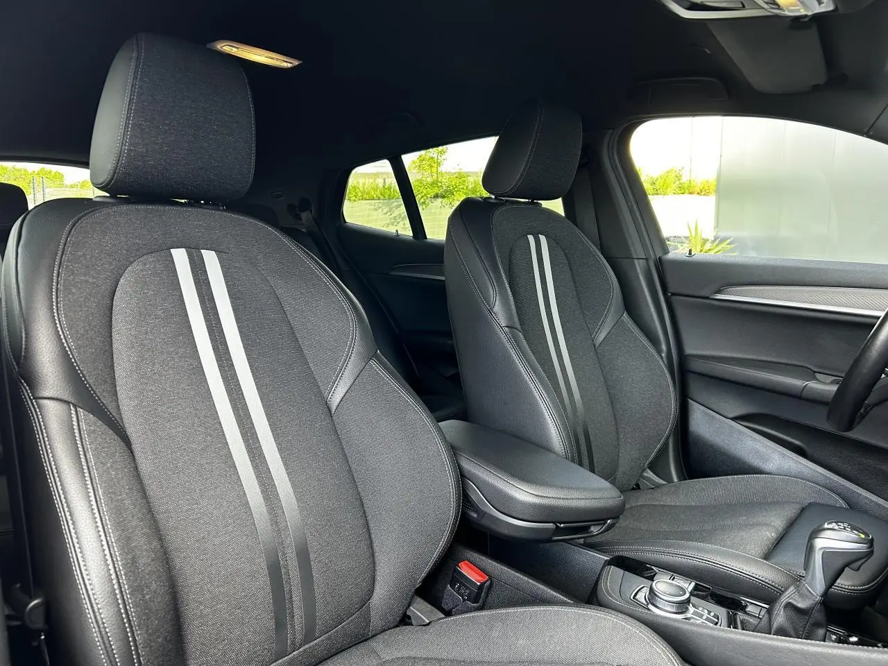 Intérieur de la BMW X2 F39 2021, vue sur les sièges avant noirs avec bandes grises et accoudoir central.