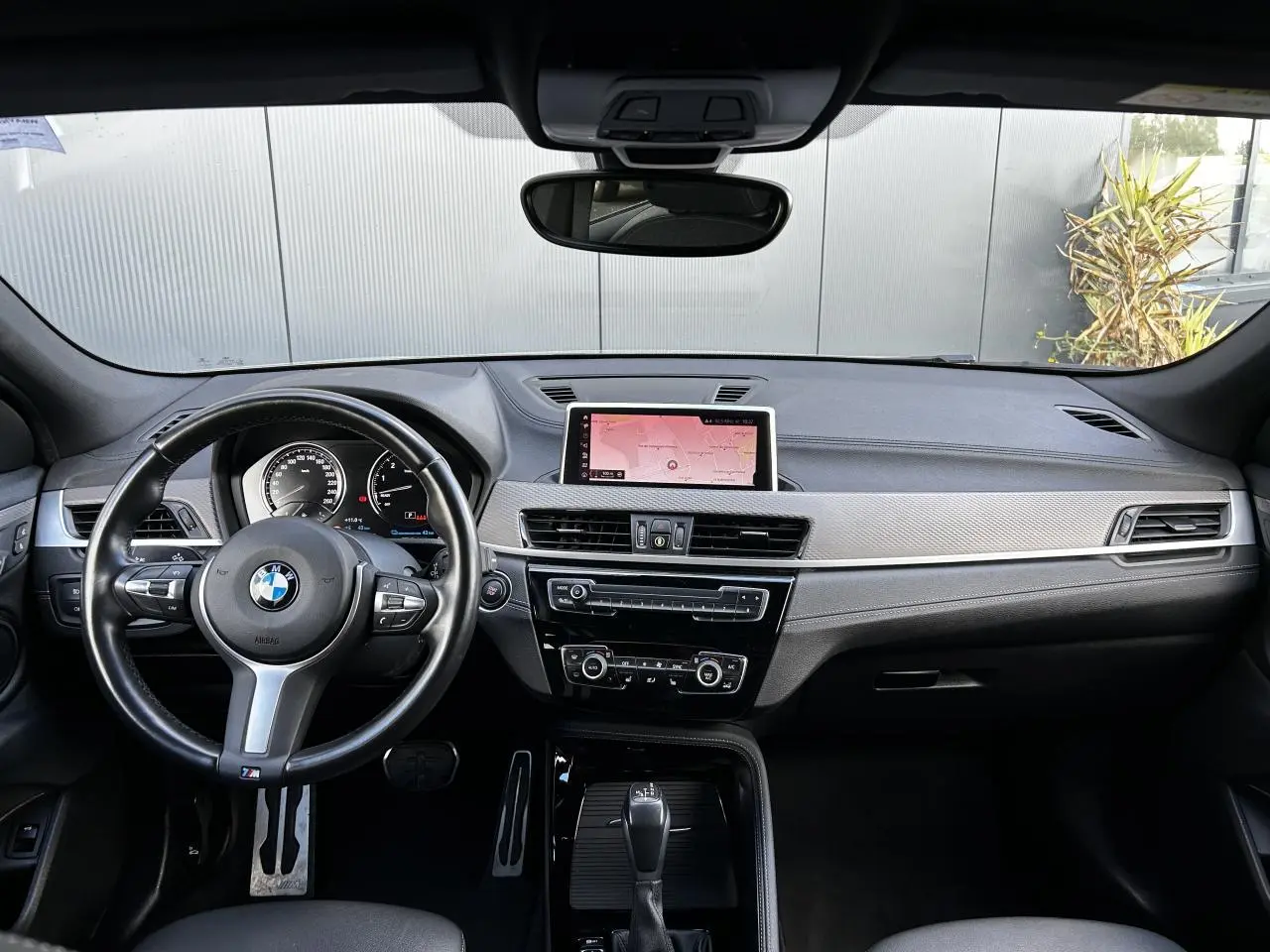 Intérieur BMW X2 F39 2021 vu de face, tableau de bord noir avec écran GPS central et volant M cuir.