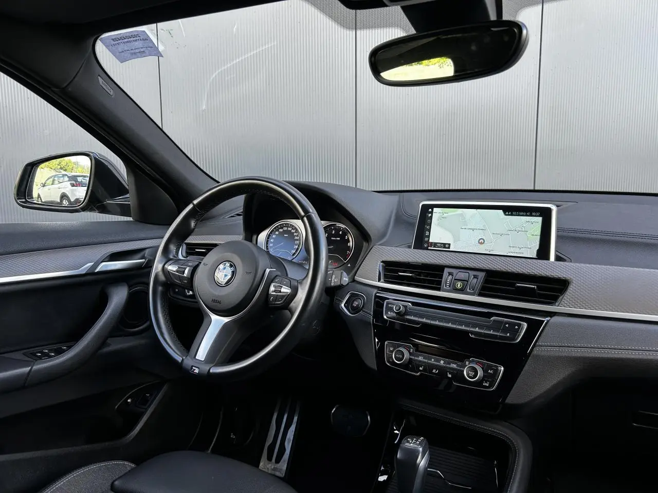 Intérieur BMW X2 F39 vu côté conducteur, tableau de bord noir avec écran GPS et volant M cuir multifonctions.