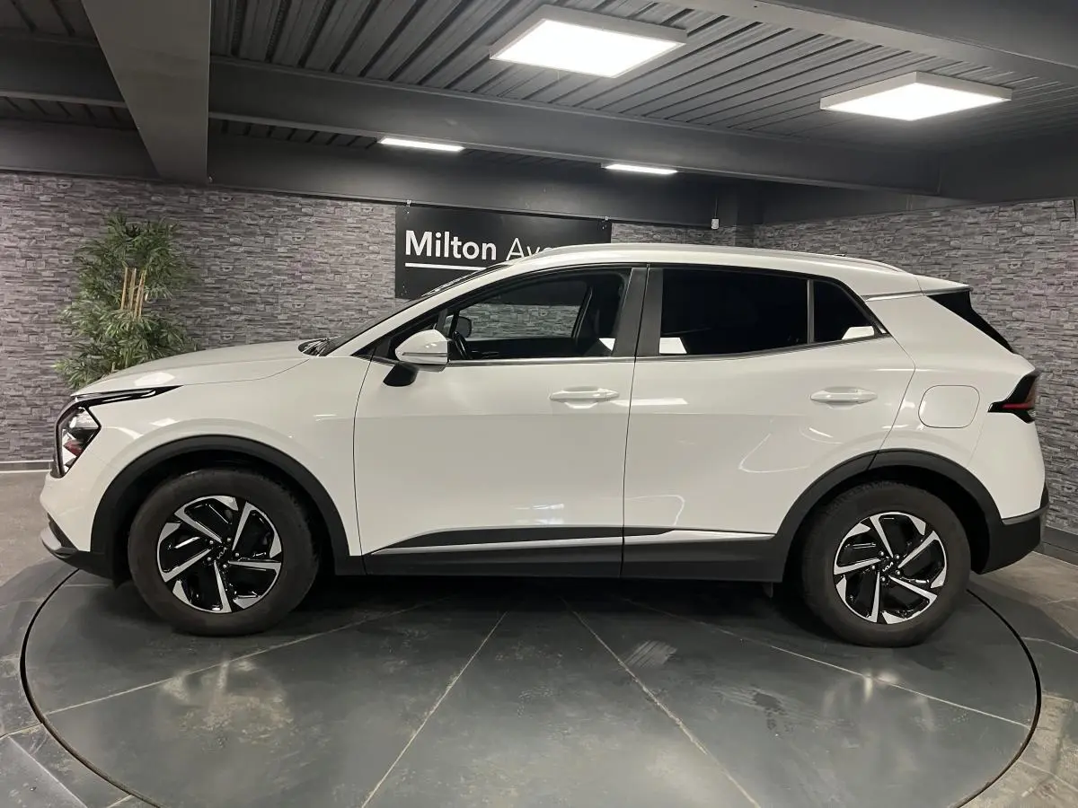 KIA SPORTAGE blanc nacré vu de profil côté gauche, avec jantes alliage noires et vitres surteintées.