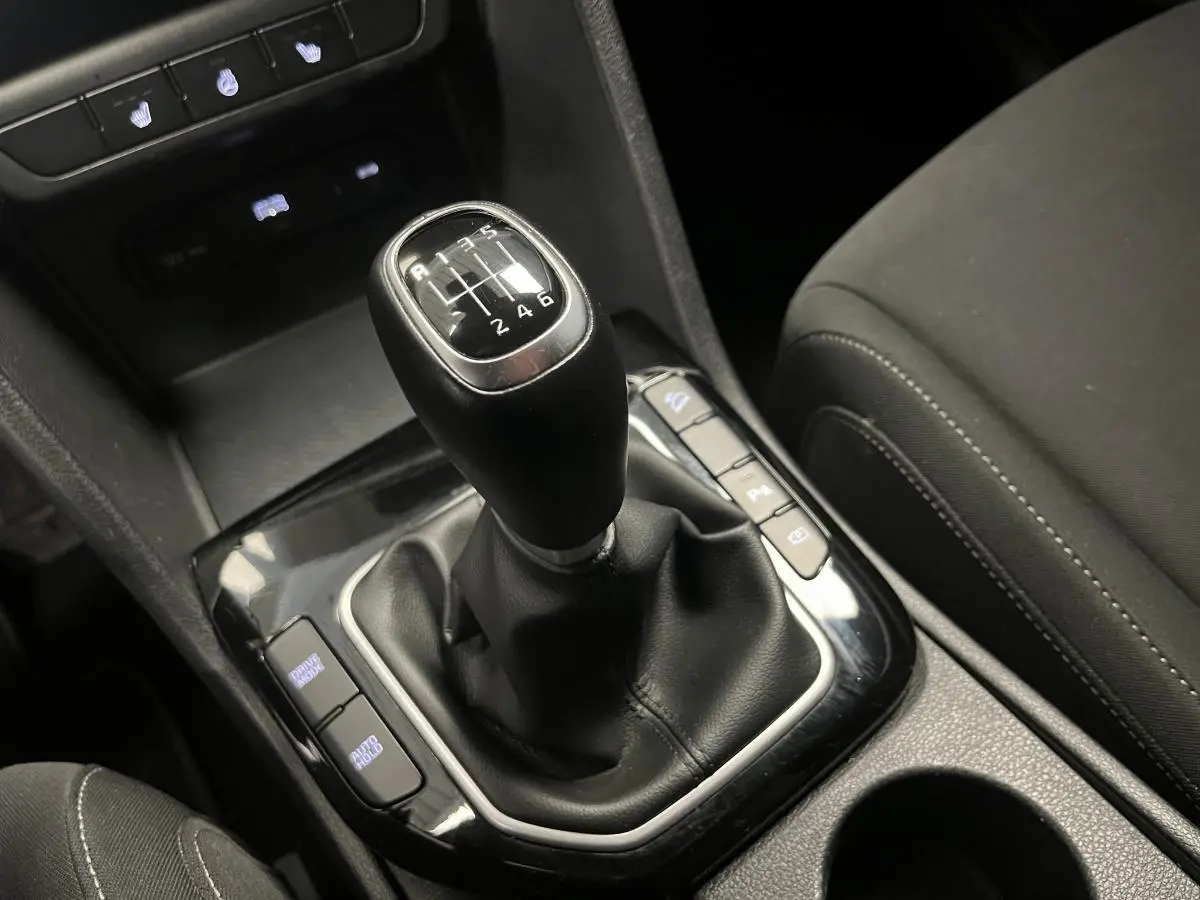 Le levier de vitesses manuel noir du Kia Sportage 2022, entouré de commandes et accoudoir tissu gris.