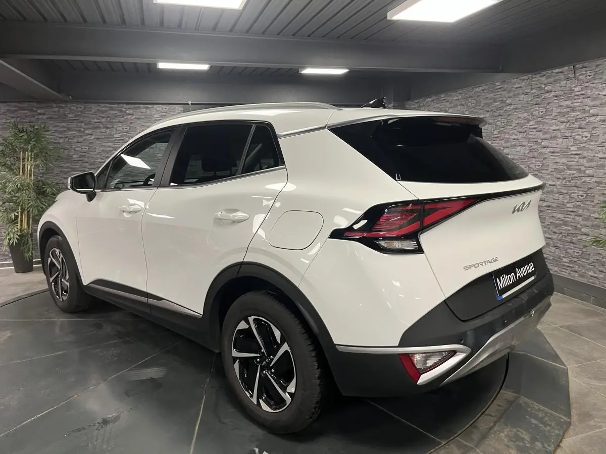 Vue 3/4 arrière droite d'un KIA Sportage blanc nacré avec jantes alliage 18 pouces et feux arrière LED boomerang.