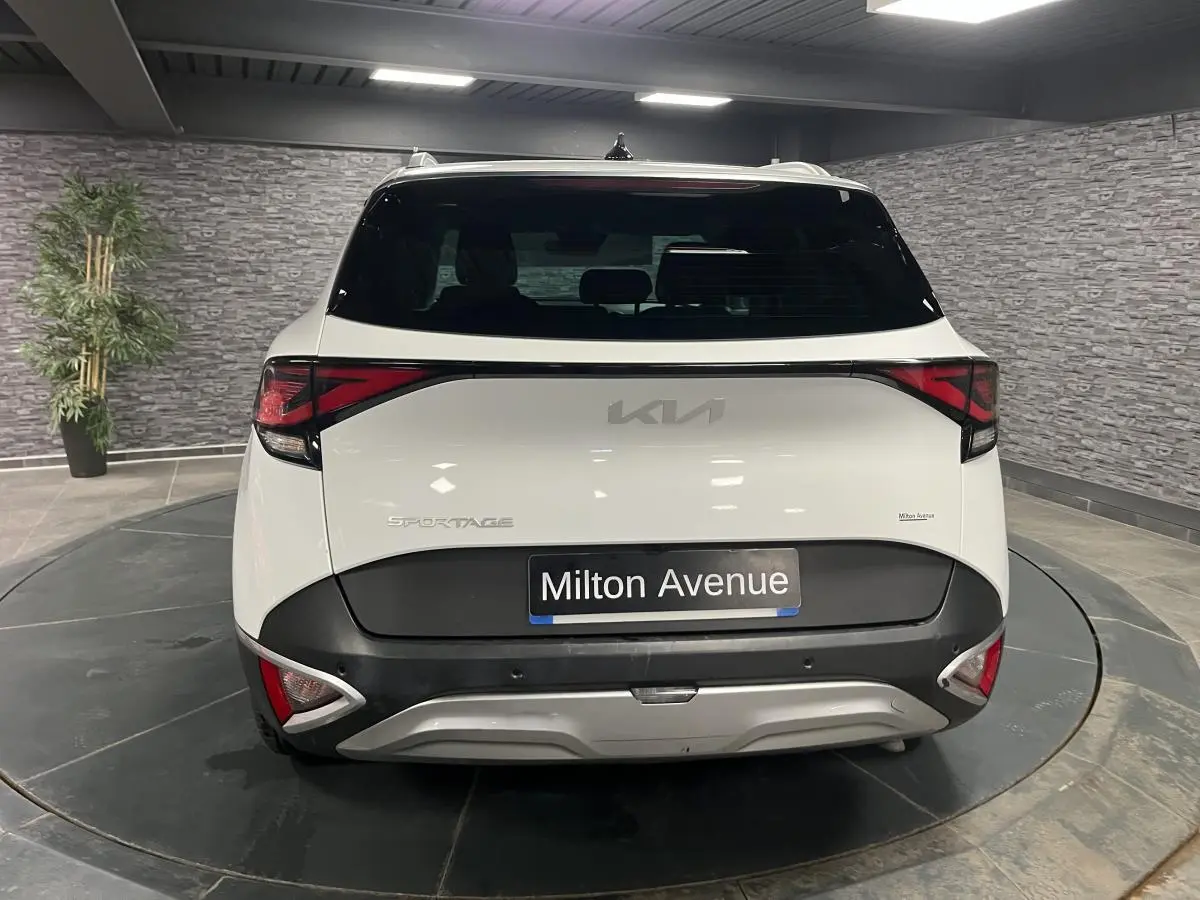 Vue arrière du KIA Sportage blanc nacré avec bouclier noir laqué et feux arrière LED en intérieur showroom.