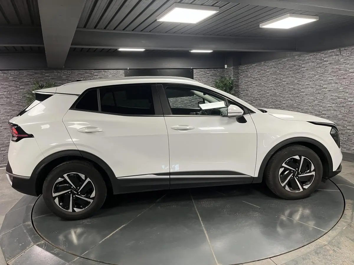 Profil côté gauche d'un KIA SPORTAGE blanc nacré 2022 avec jantes alliage 18 pouces et vitres surteintées.