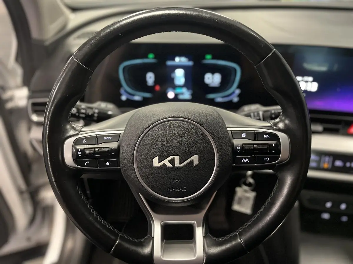 Volant cuir noir du Kia Sportage 2022 avec commandes intégrées et tableau de bord digital en arrière-plan.
