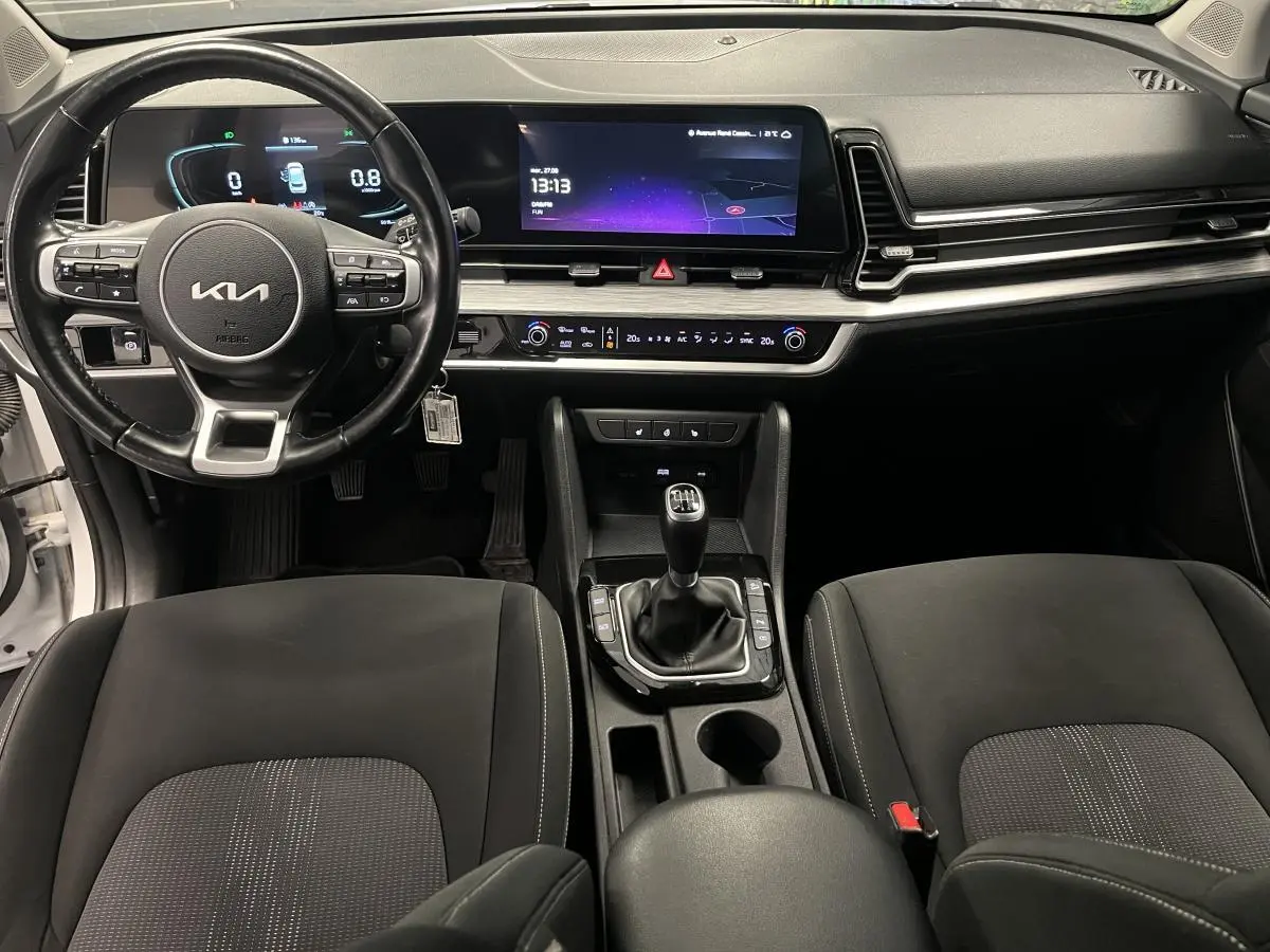Intérieur du Kia Sportage 2022 vue avant, tableau de bord noir avec écran tactile et levier de vitesses manuel.