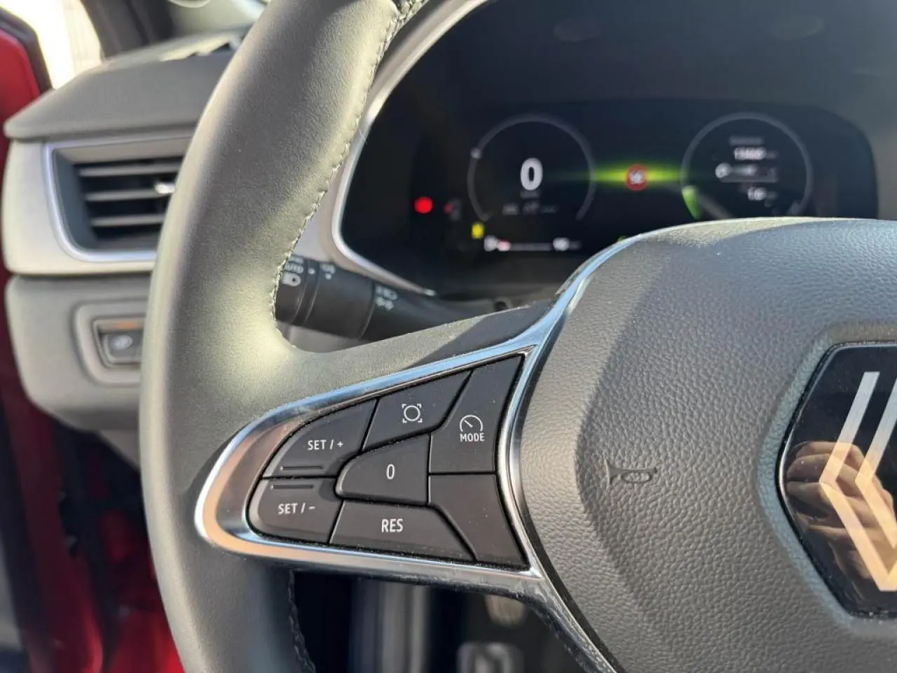 Gros plan sur le volant côté gauche du Renault Captur II Rouge Flamme avec commandes intégrées et tableau de bord numérique flou.