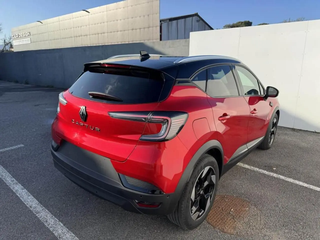 Vue 3/4 arrière droite d'un Renault Captur II rouge flamme avec toit noir et jantes noires en aluminium.
