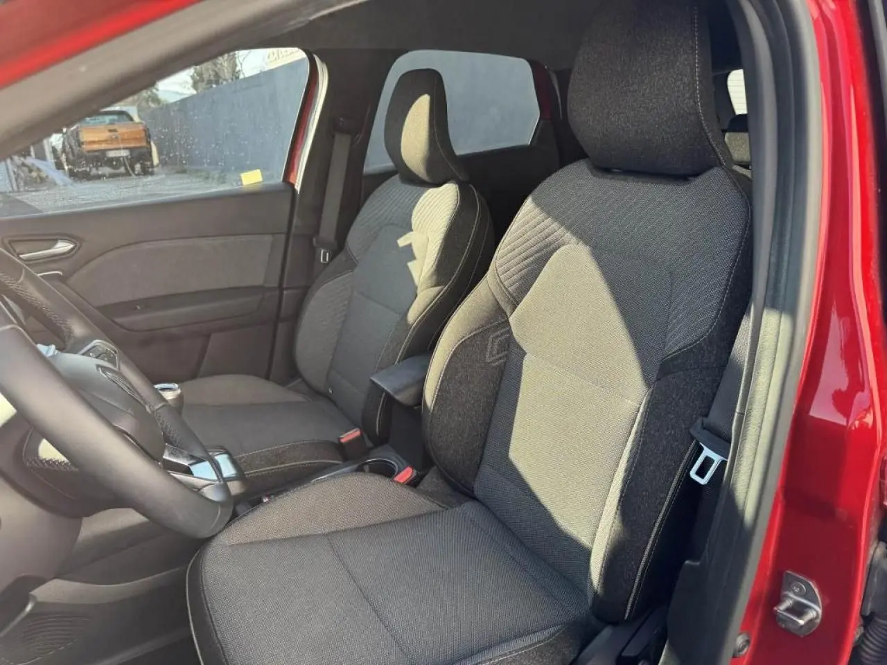 Vue intérieure côté gauche des sièges avant gris foncé du Renault Captur II rouge flamme avec accoudoir central.