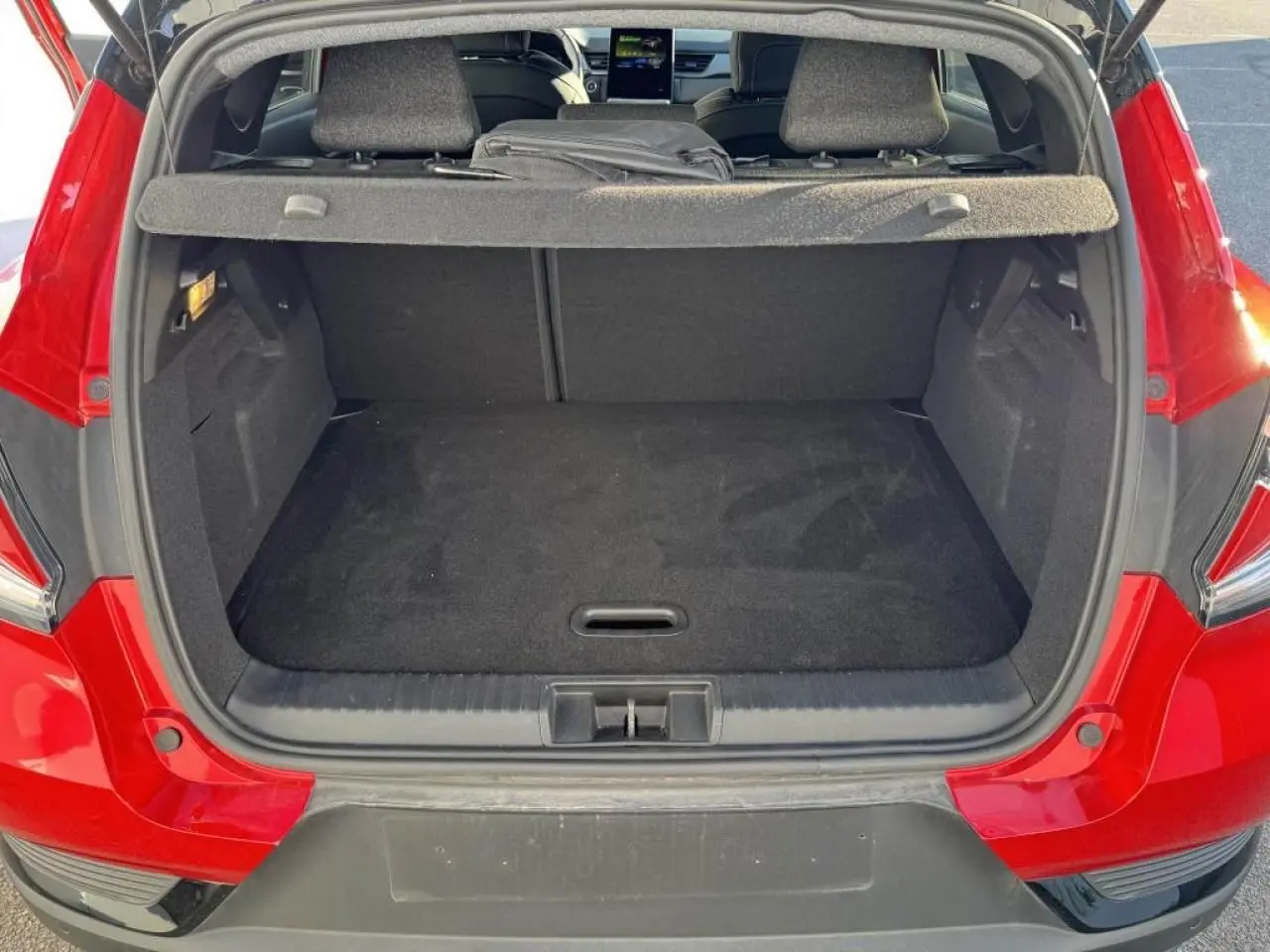 Coffre ouvert vu de l'arrière d'un Renault Captur rouge flamme avec toit noir, montrant l'espace de chargement vide.