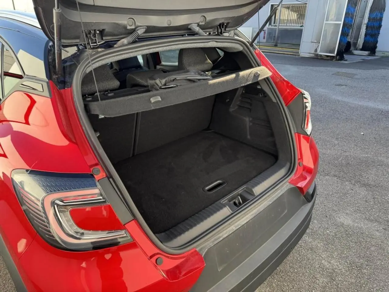 Coffre ouvert en vue arrière d’un Renault Captur II rouge flamme avec toit noir, montrant l’espace de chargement vide.