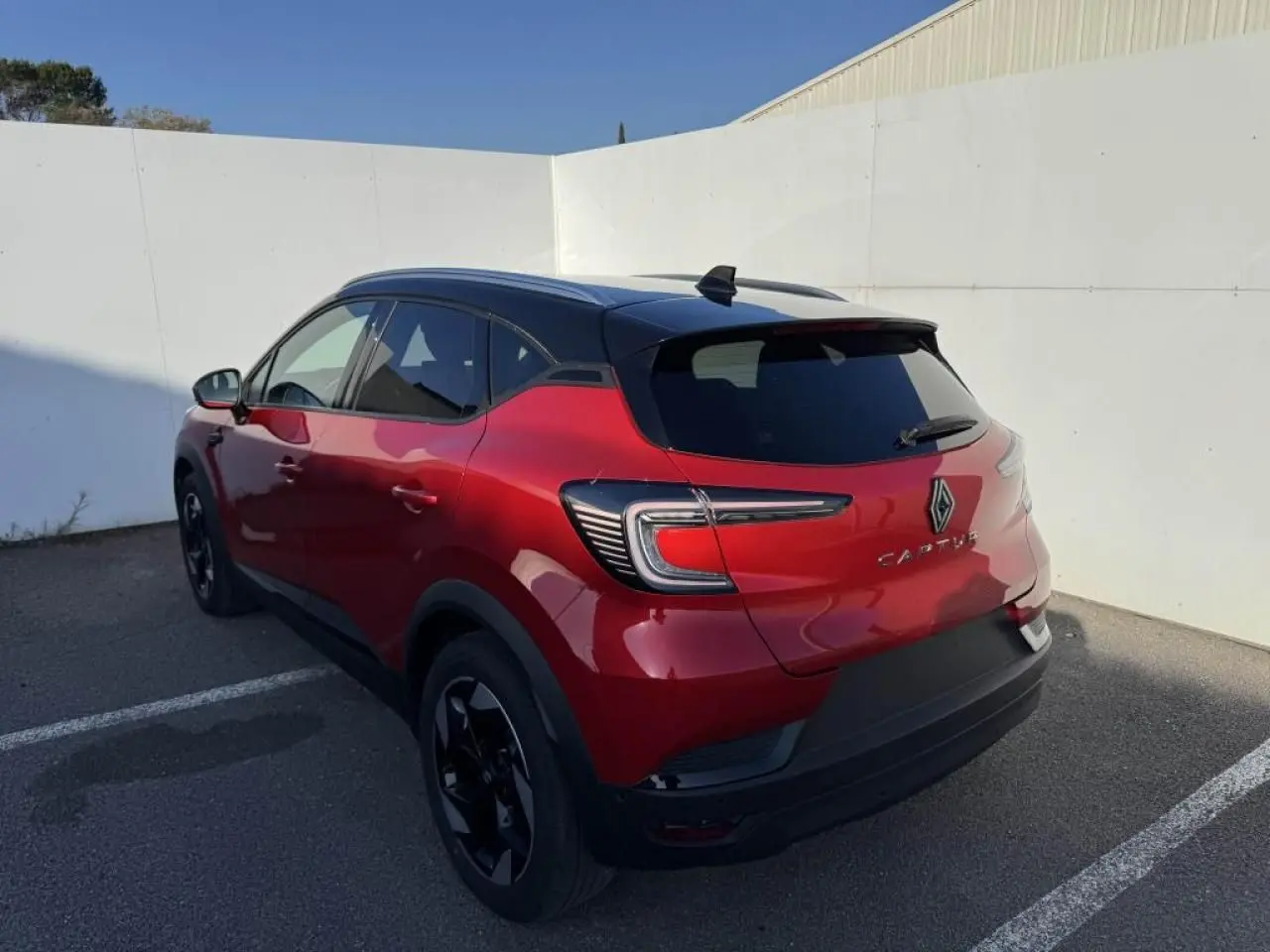 Vue 3/4 arrière droite d’un Renault Captur rouge flamme avec toit noir et jantes noires, stationné en extérieur.