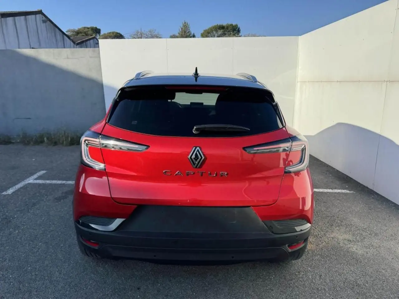 Vue arrière du Renault Captur II rouge flamme avec toit noir, mettant en valeur ses feux LED et son logo central.