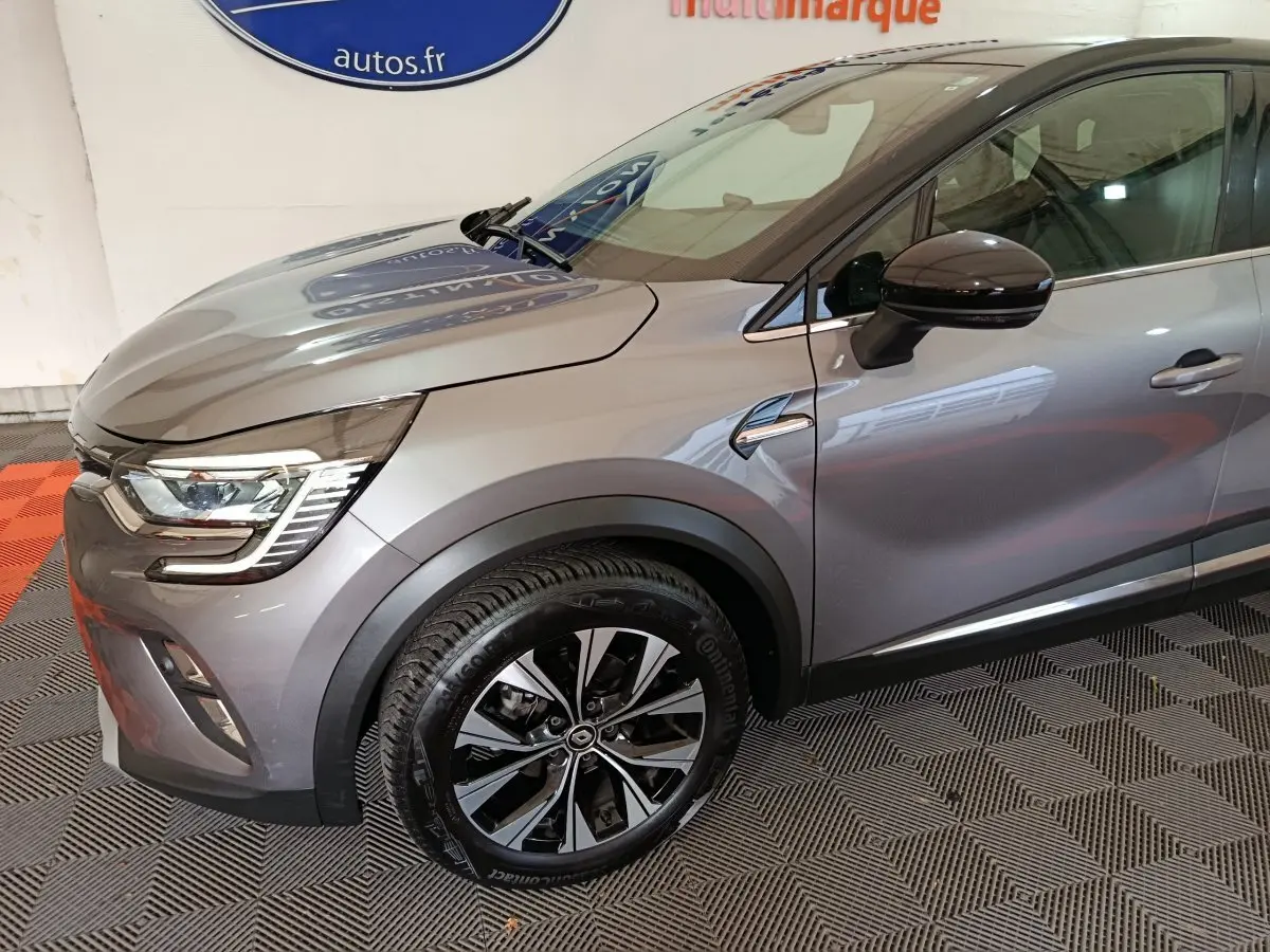 Vue de profil avant droit d'un Renault Captur techno TCe 90 gris foncé avec jante alliage et rétroviseur noir brillant.