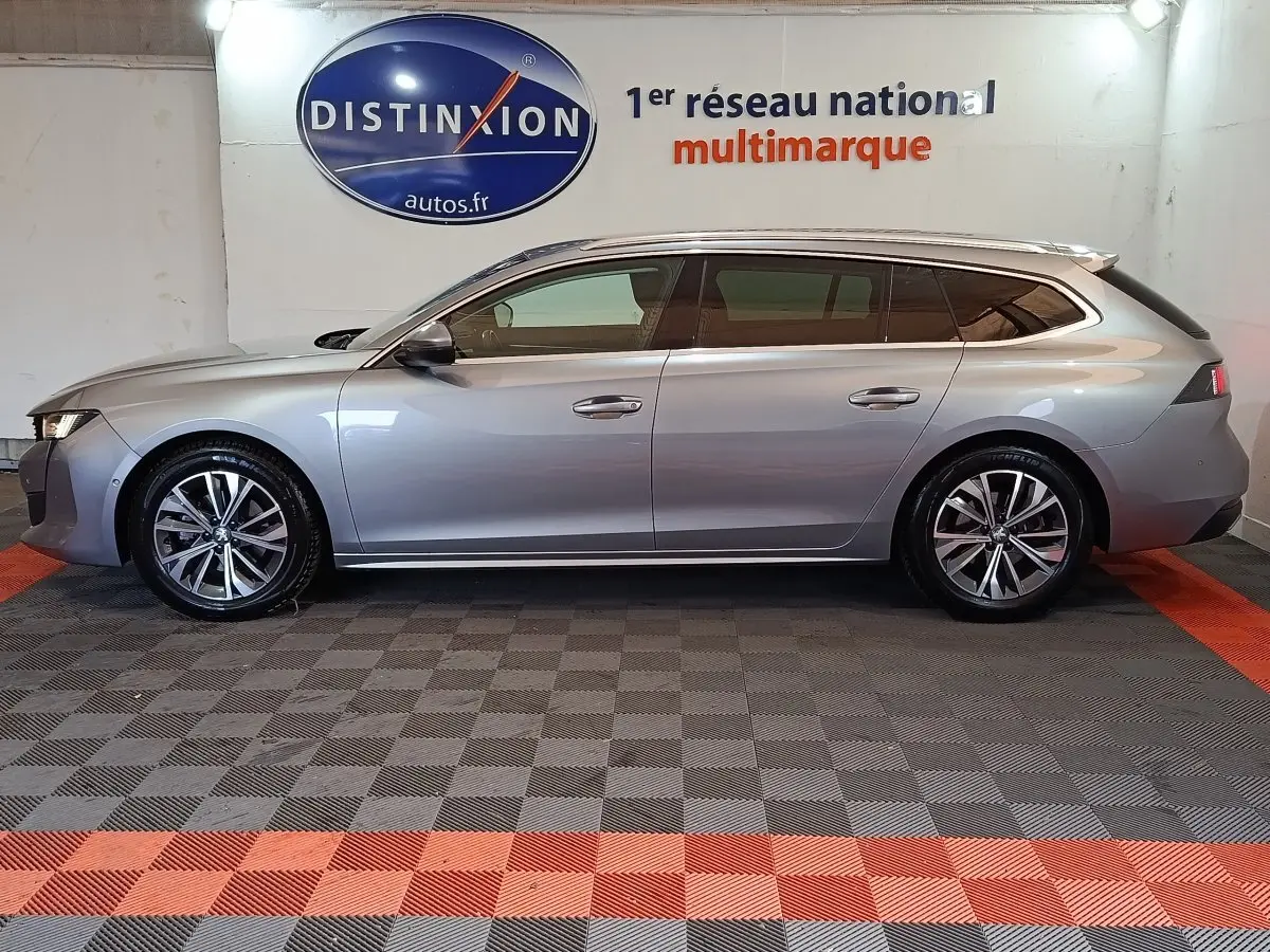 Profil droit d'une Peugeot 508 SW BlueHDi gris clair 2020 avec jantes alliage et vitres teintées, en intérieur showroom.