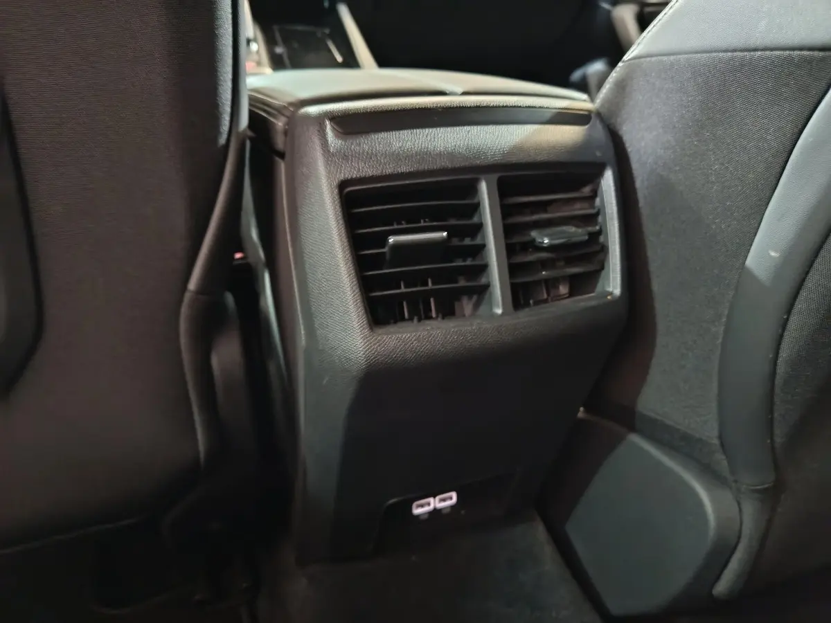 Détail des aérateurs arrière noirs et ports USB sous la console centrale entre les sièges avant d’une Peugeot 508 gris clair.