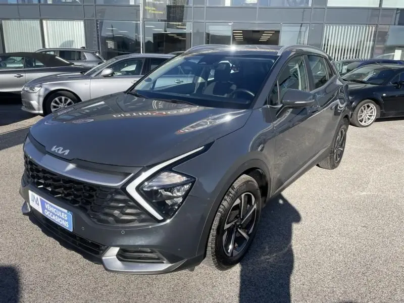 KIA Sportage gris Eclipse Metal en 3/4 avant droit, avec calandre noire et feux LED distinctifs, stationné en extérieur.