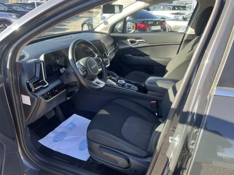 Vue intérieure côté conducteur du Kia Sportage gris Eclipse Metal 2023, avec tableau de bord moderne et sièges tissu noirs.