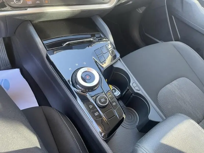Vue rapprochée de la console centrale noire brillante du Kia Sportage 2023 avec molette de sélection de vitesse et porte-gobelets.