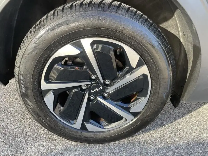 Gros plan sur la jante alliage bicolore noire et argentée avec logo KIA, montée sur un pneu Bridgestone du Kia Sportage gris eclipse.