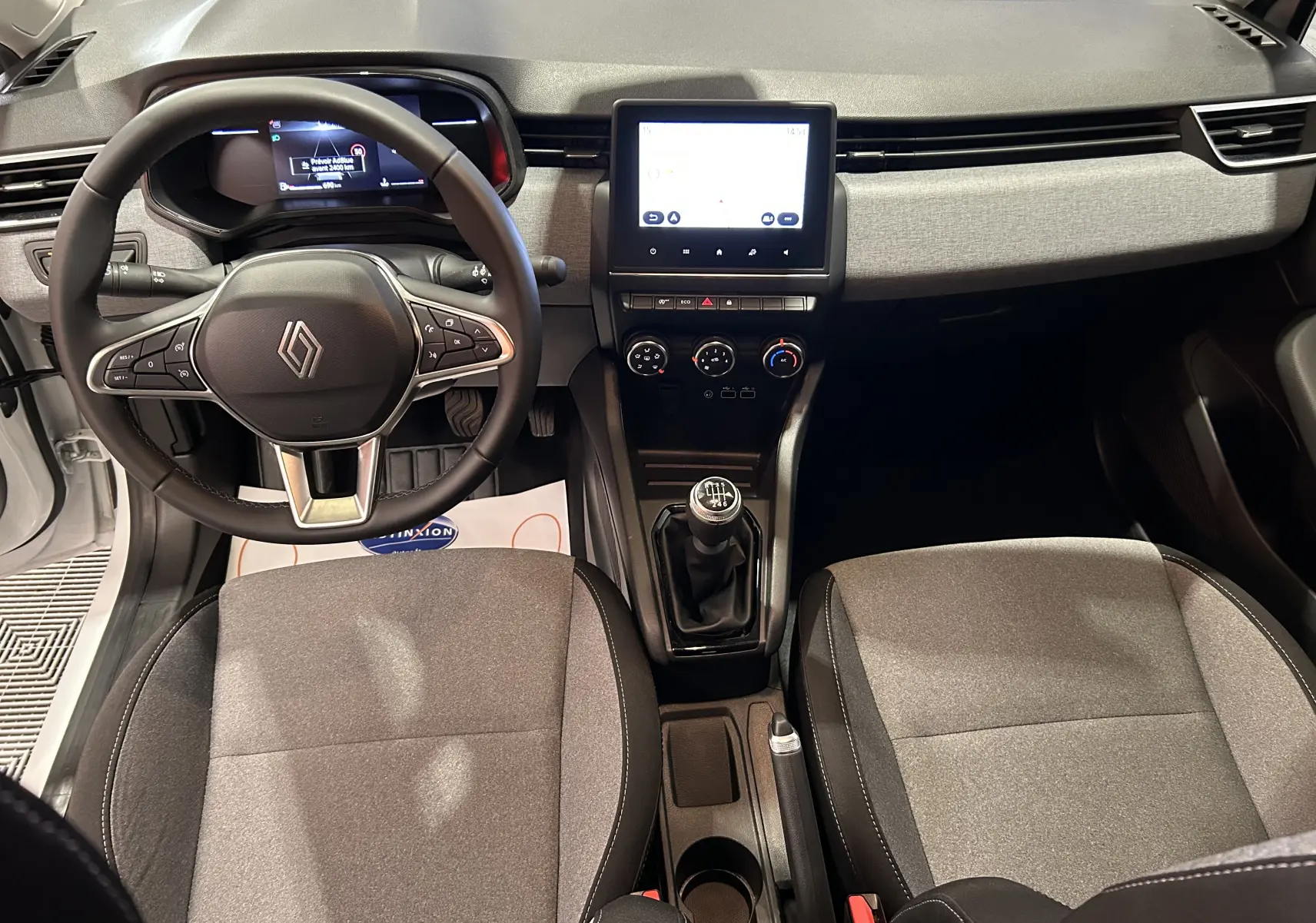 Vue intérieure frontale du poste de conduite de la Renault Clio V blanche avec volant multifonction et boîte manuelle.