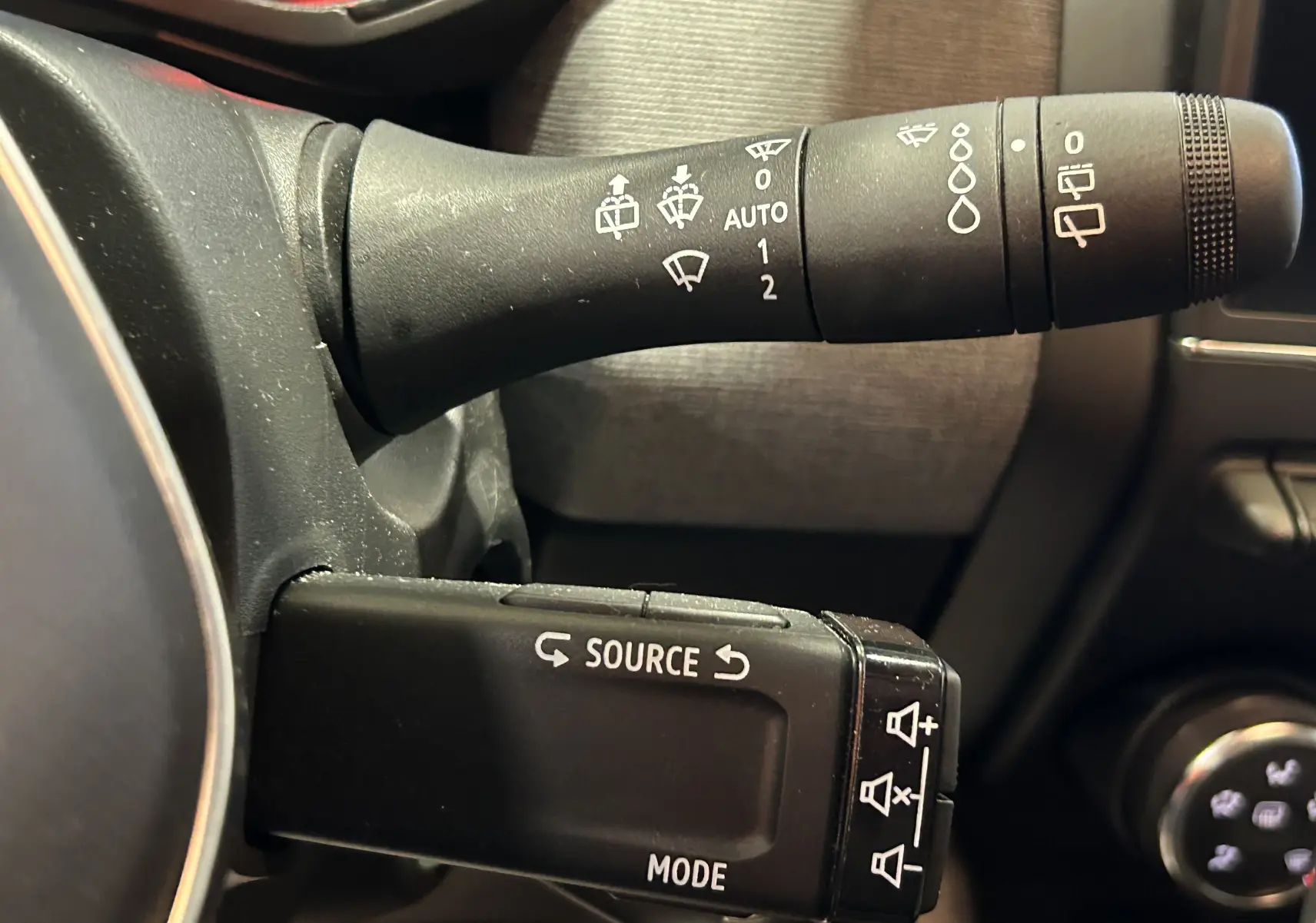 Gros plan sur les commandes de lève-glace et multimédia noires à gauche du volant dans l’habitacle de la Renault Clio V blanche.