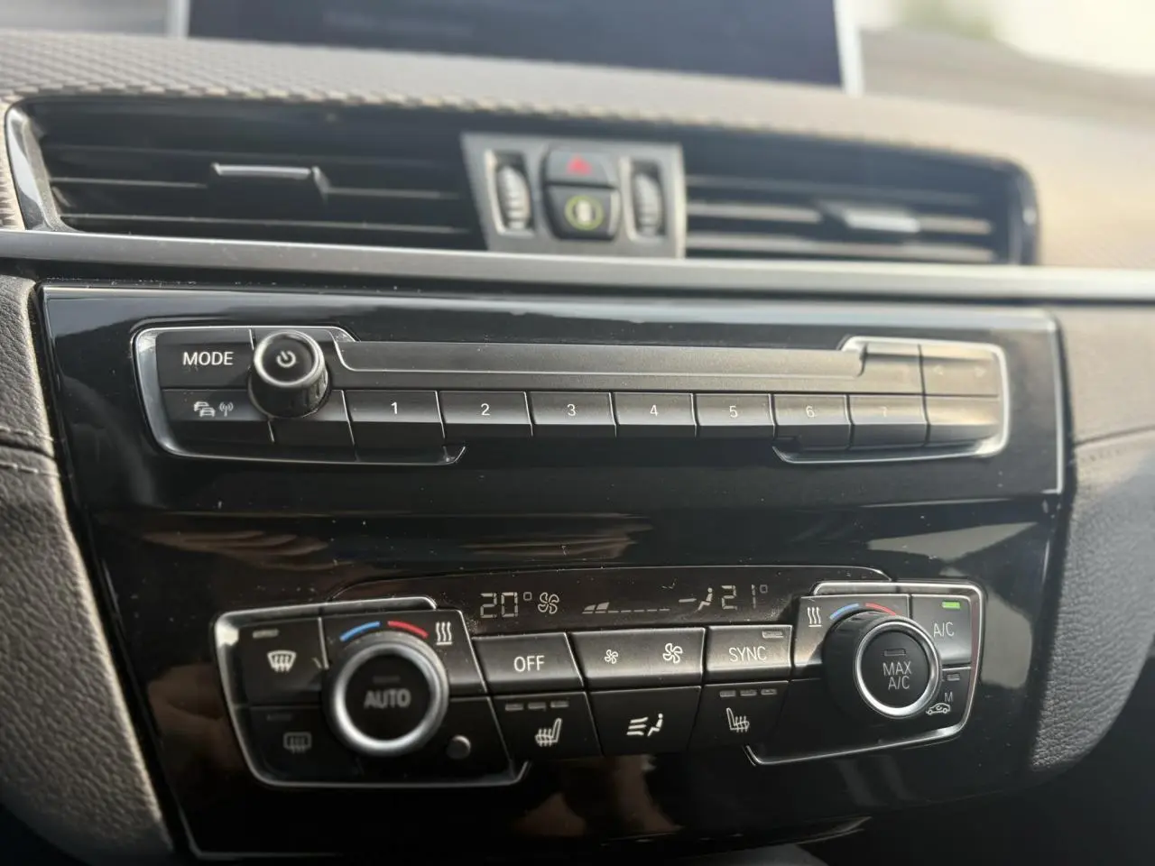 Tableau de bord noir brillant de BMW X2 F39, vue rapprochée sur commandes climatisation automatique et multimédia.