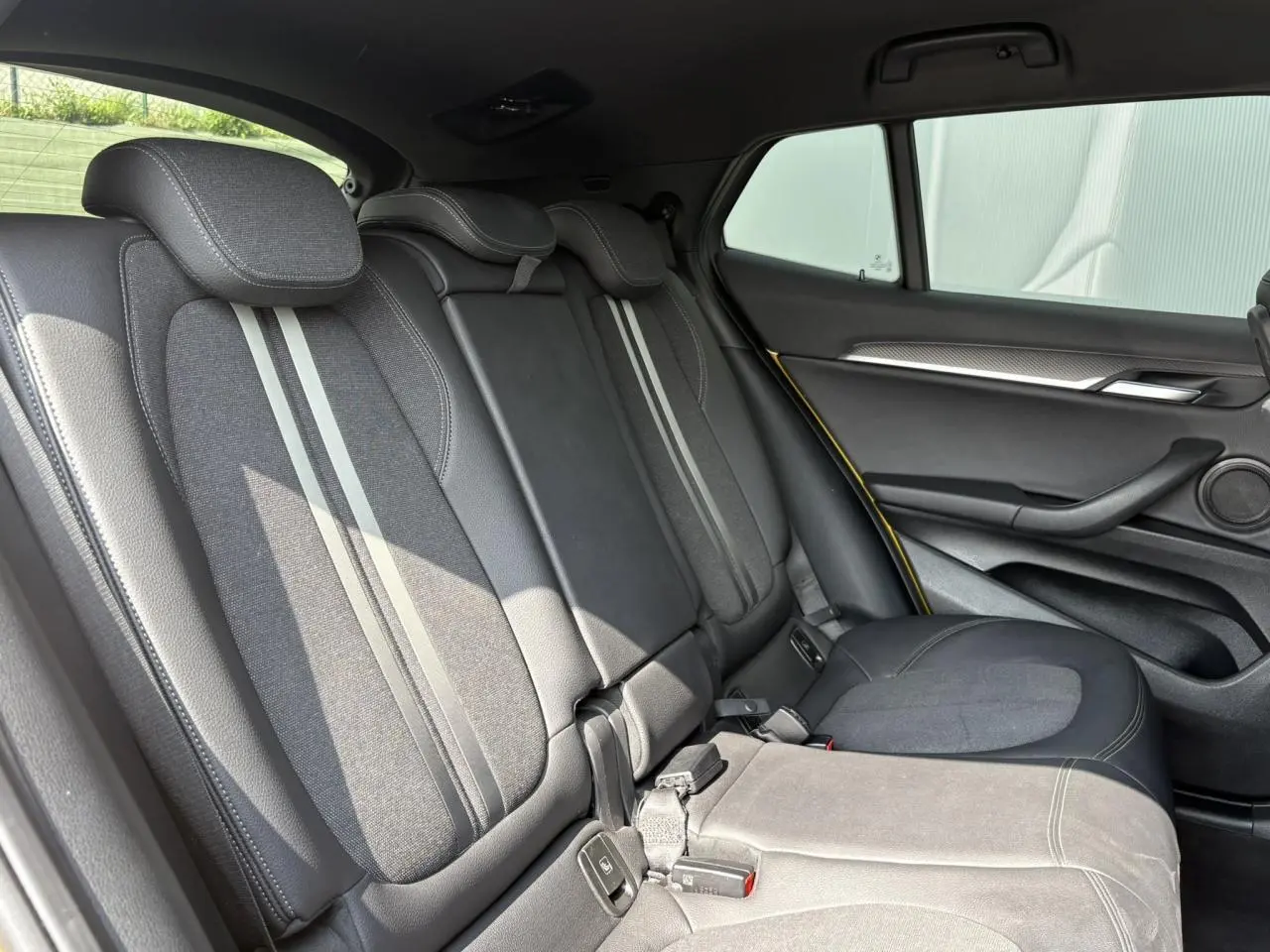 Vue latérale droite de l'intérieur arrière du BMW X2 F39 avec sièges en tissu gris et cuir noir, détails jaunes sur la porte.