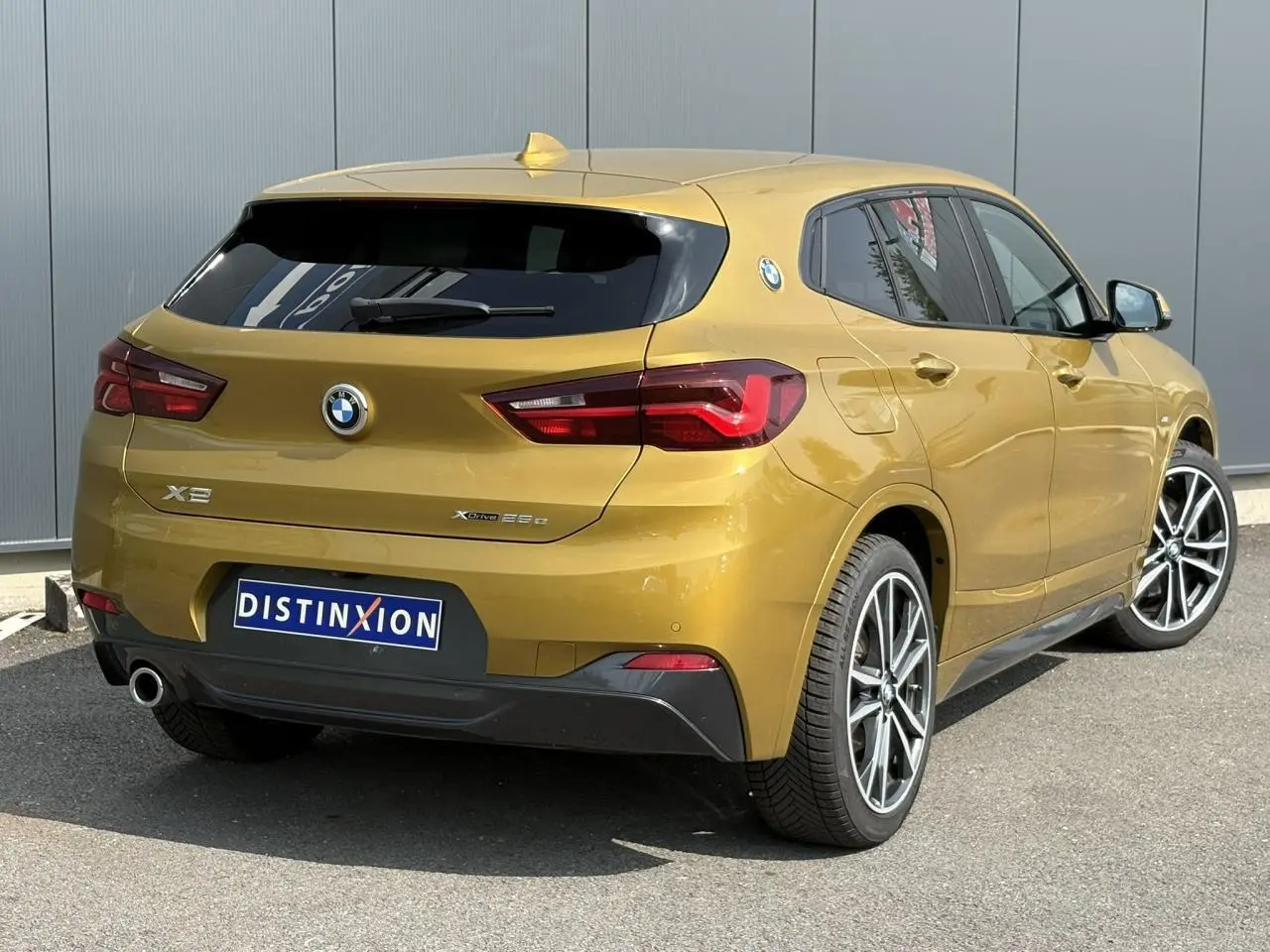 Vue 3/4 arrière droite d'un BMW X2 F39 xDrive 25e or Galvanic avec jantes alliage bicolores et hayon électrique.