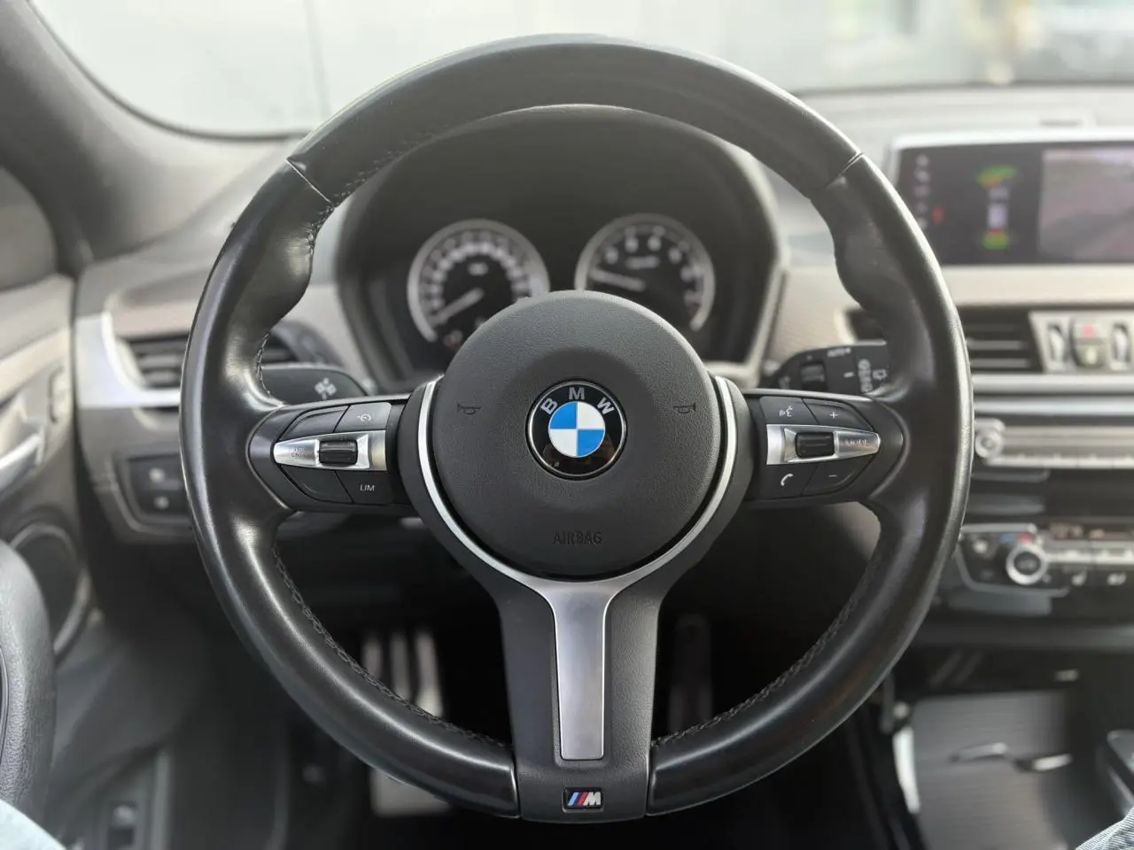 Volant M en cuir noir de BMW X2 F39, vue frontale centrée sur les commandes multifonctions et le tableau de bord flou.