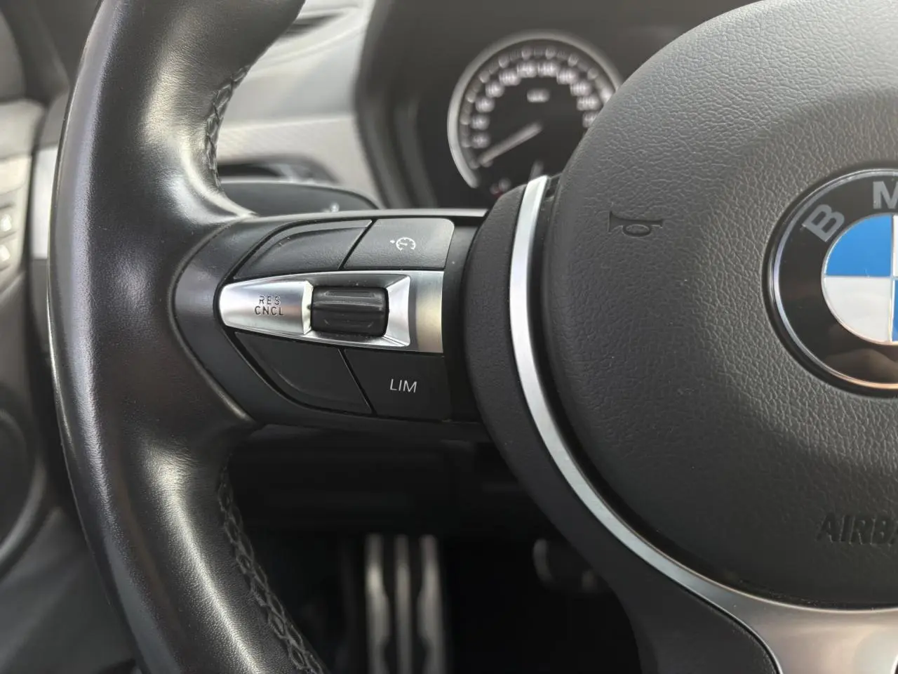 Gros plan sur le volant cuir noir du BMW X2 F39, avec commandes multifonctions et logo BMW visible au centre.