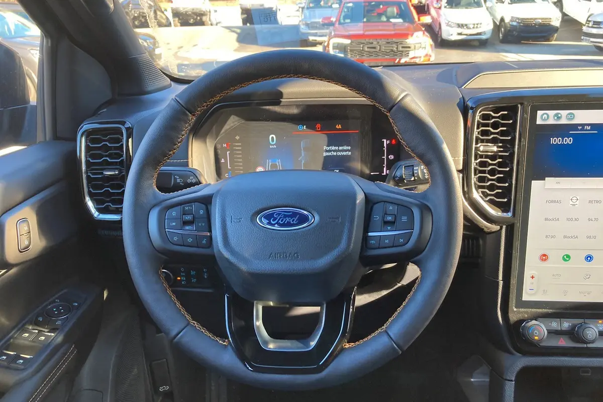 Vue intérieure centrée sur le volant en cuir avec surpiqûres marron du Ford Ranger 2025 Bleu Lightning, tableau de bord numérique visible.
