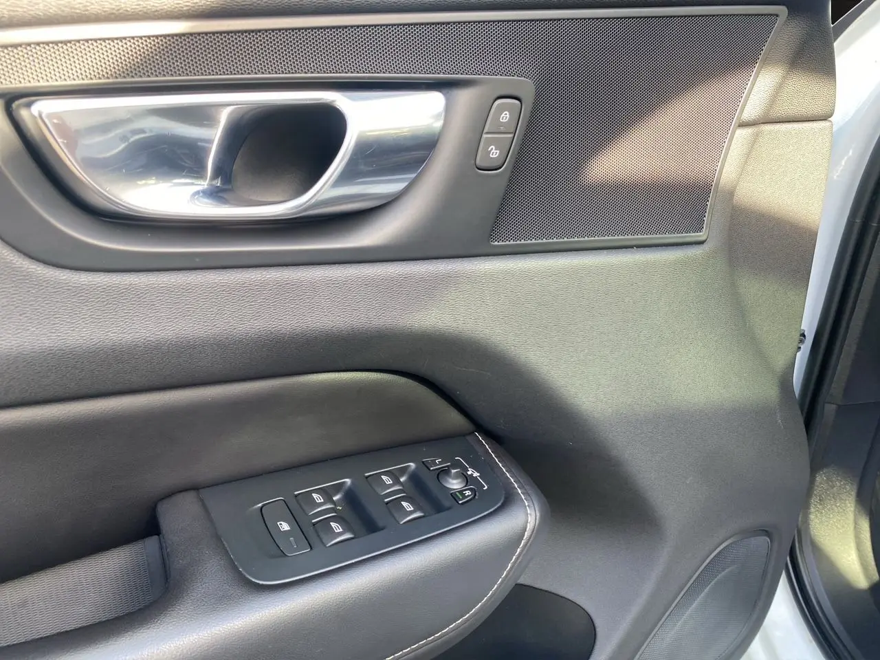 Gros plan sur la porte avant gauche du Volvo XC60 blanc 2019, montrant les commandes de vitres et la poignée intérieure chromée.
