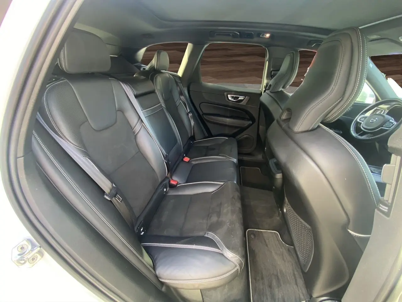 Intérieur arrière du Volvo XC60 blanc 2019, sièges cuir noir avec surpiqûres blanches, vue côté gauche depuis la porte ouverte.